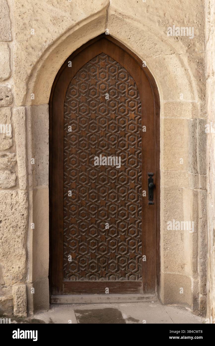 Foto verticale di una splendida porta in legno fatta a mano inserita all'interno di un arco in pietra, che mostra intricati motivi geometrici e un classico de architettonico Foto Stock