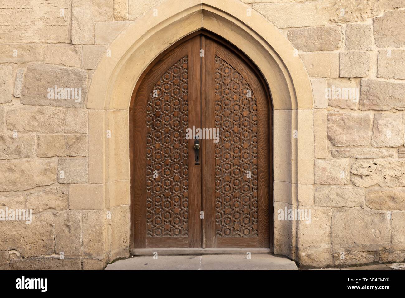 Splendida porta in legno realizzata a mano all'interno di un dettagliato arco in pietra, che mostra intricati motivi geometrici e classici dettagli architettonici suita Foto Stock