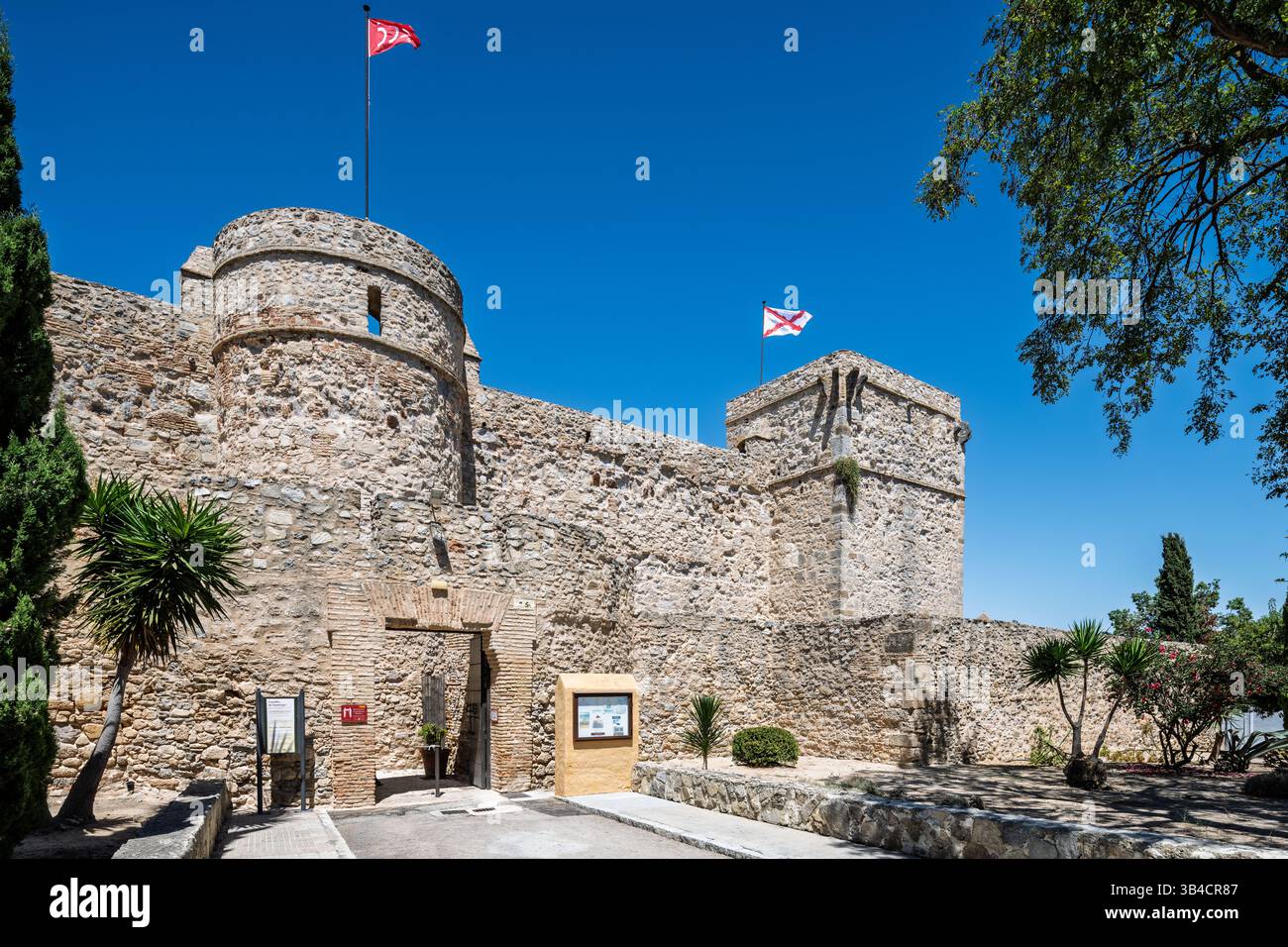 I visitatori ammirano lo storico castello di Santiago a Sanlucar de Barrameda, in Spagna, contro un cielo azzurro e una vegetazione vivace. Foto Stock