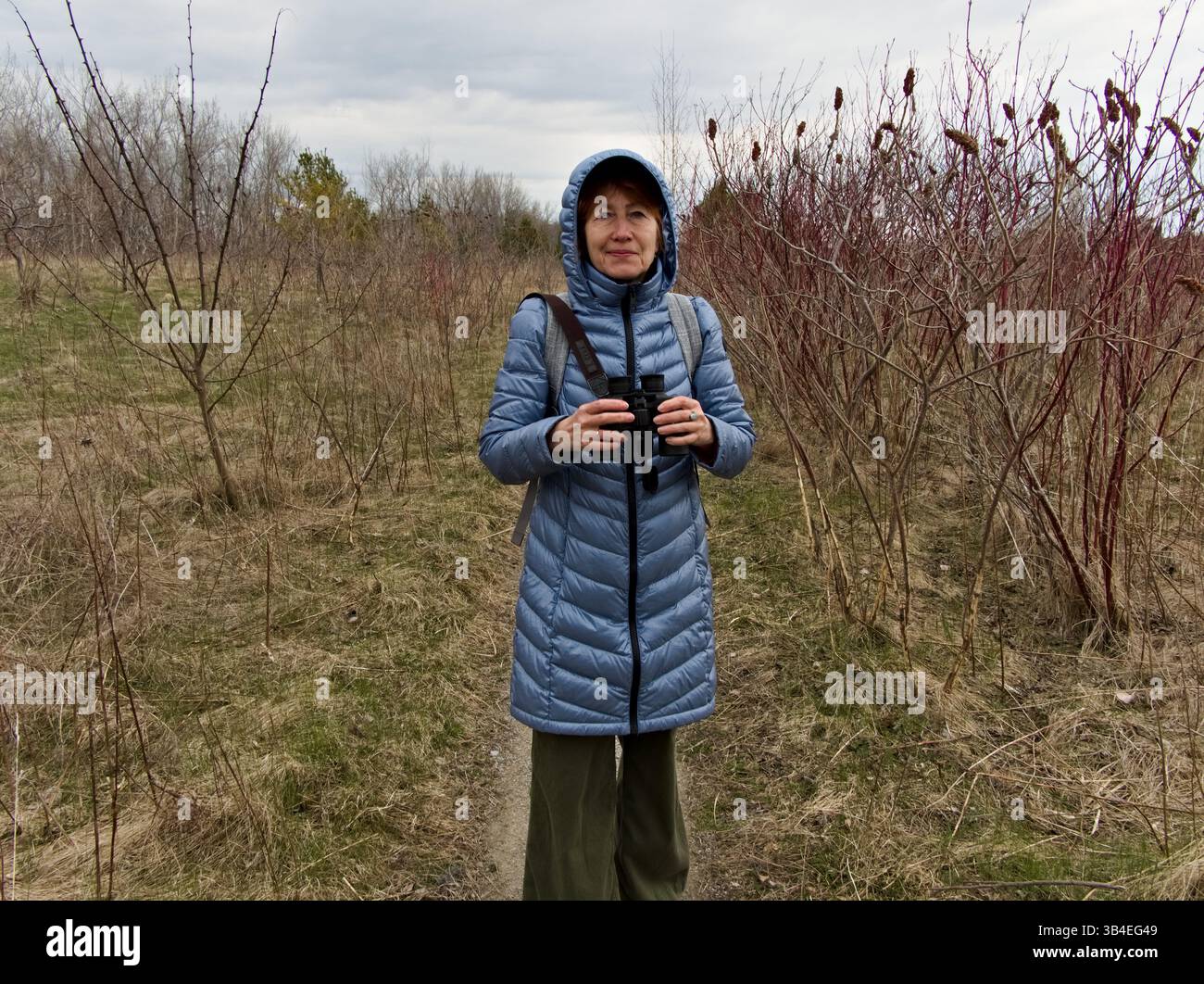 La donna rimane immobile, scansionando attentamente gli uccelli nella foresta e nel prato sparso di inizio stagione. Foto Stock
