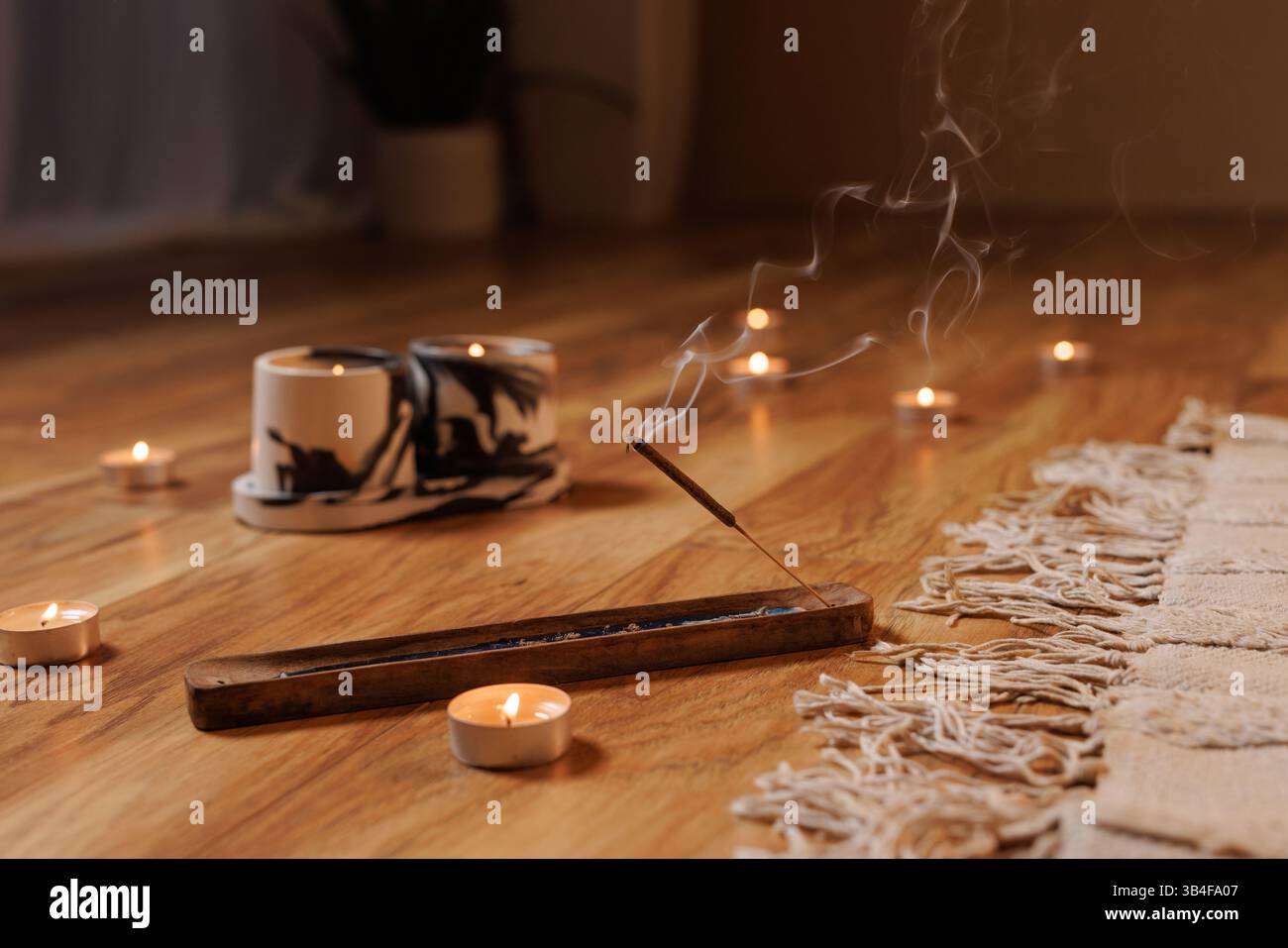 Primo piano di incenso bruciato con candele su pavimento in legno, creando un'atmosfera tranquilla e meditativa per yoga, relax o pratiche di consapevolezza. Foto Stock