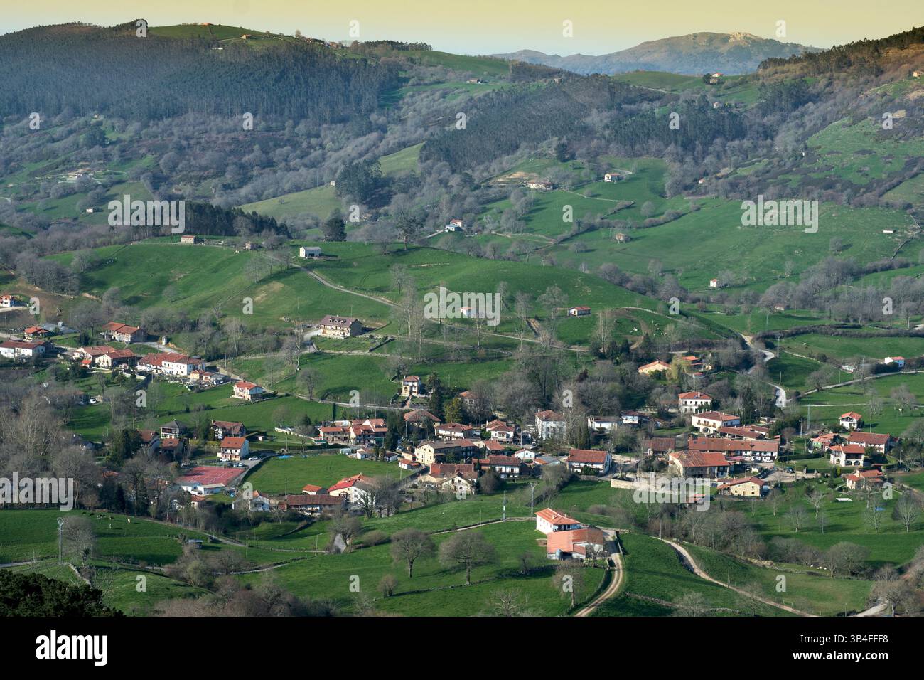 Idilliaco paesaggio di campagna che mostra colline verdi ondulate e un affascinante villaggio annidato in una valle. Esles, santa maria de Cayon, cantabria, spagna Foto Stock