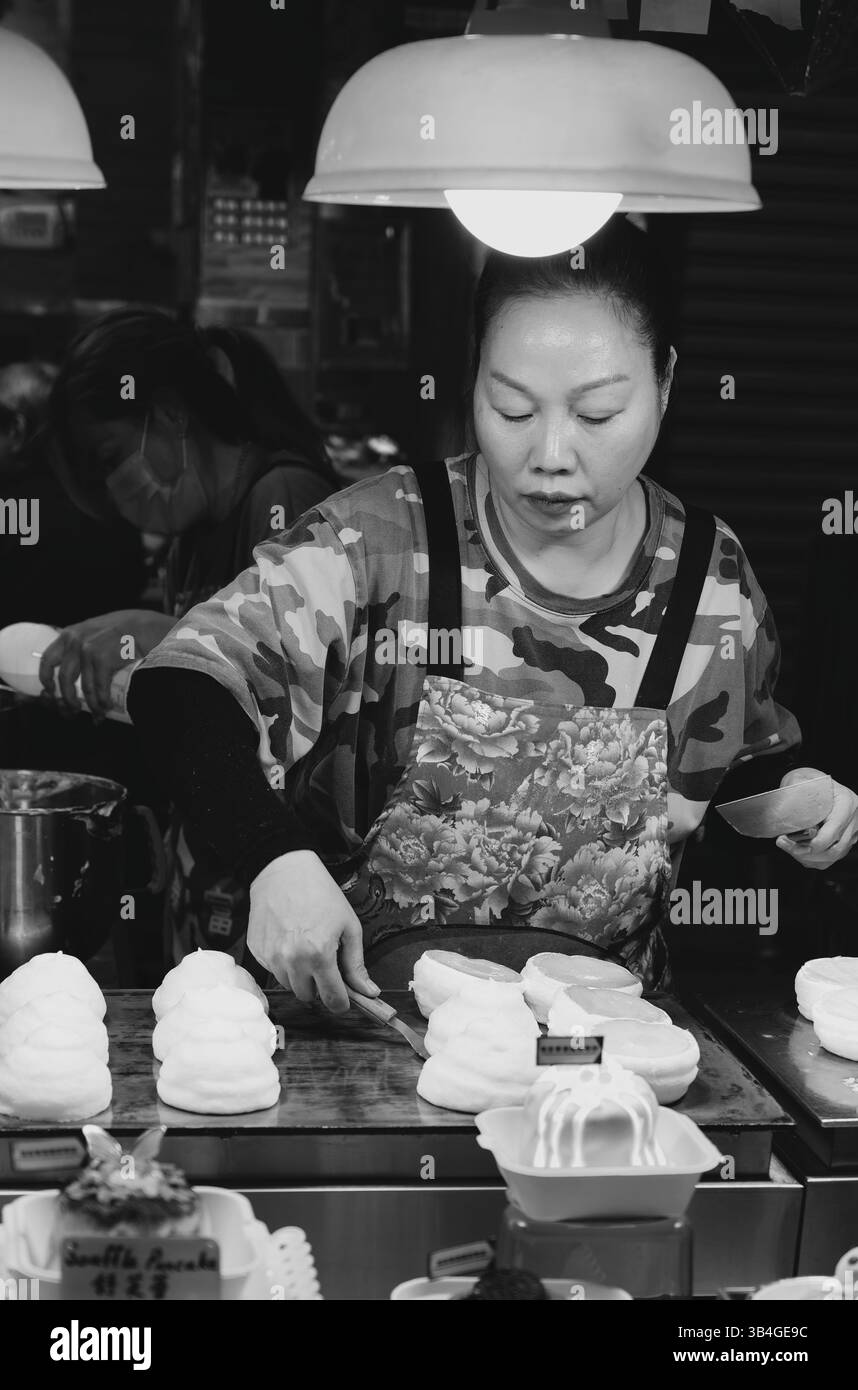 In questa scena di Street food bianco e nero, un fornitore attento lancia morbide frittelle sotto una singola lampadina Foto Stock