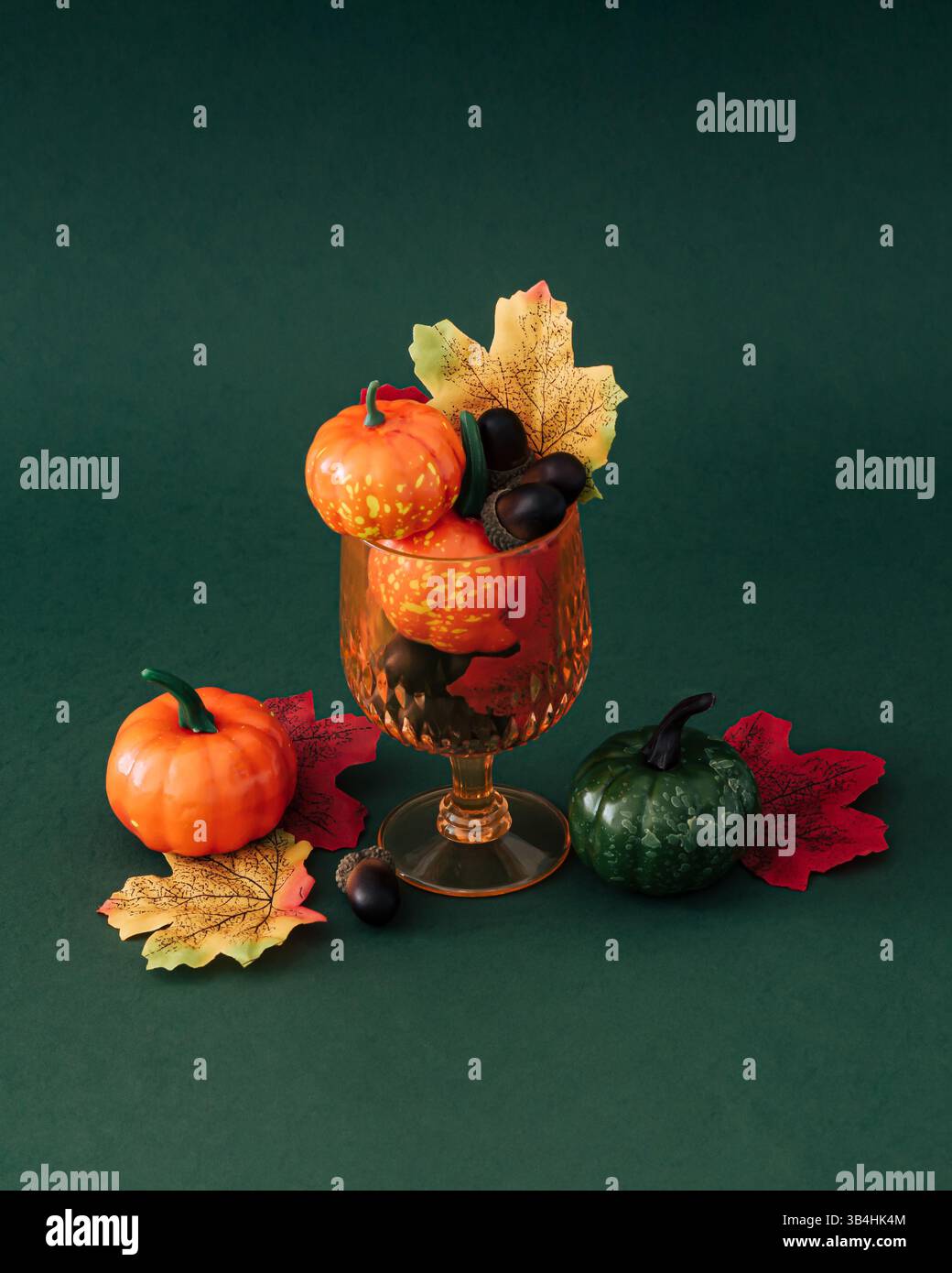 Scena autunnale di un bicchiere da cocktail pieno di foglie autunnali colorate, zucche e noci su sfondo verde. Un concetto di festa autunnale minimalista e creativo. Foto Stock