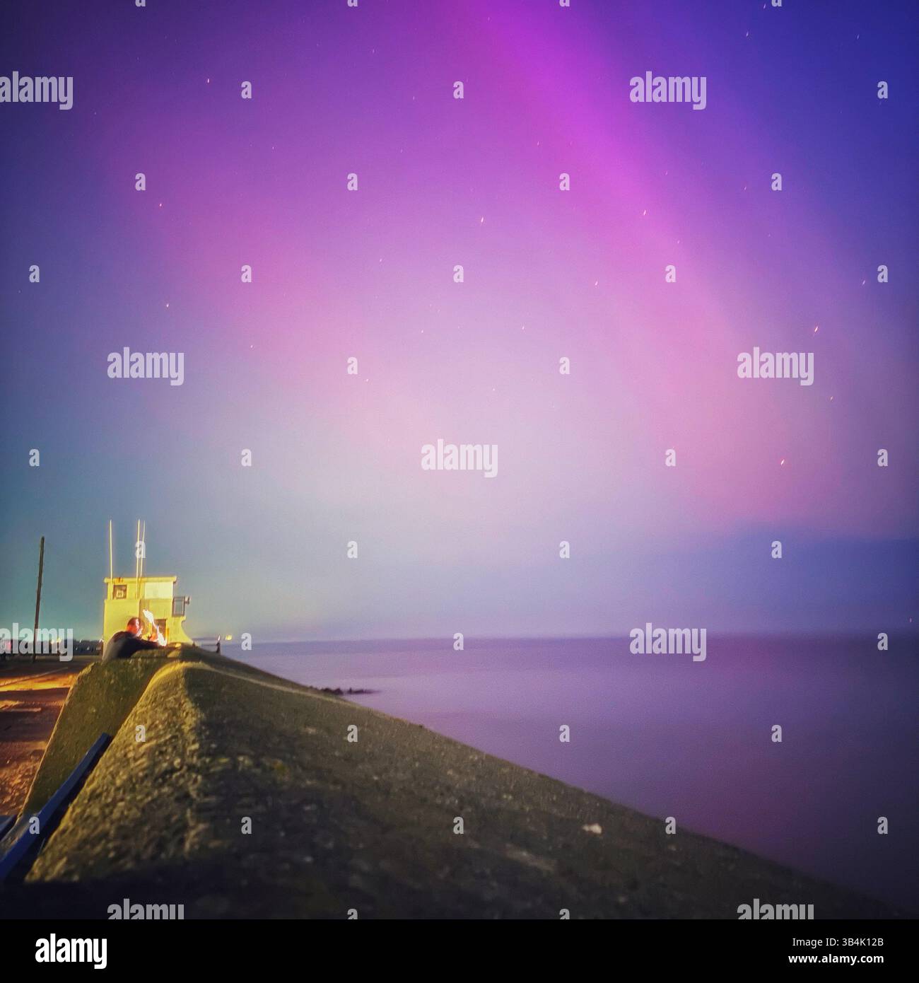 La vibrante aurora boreale sul mare calmo nel Regno Unito, mostra rare sfumature di rosa, verde e blu durante un'importante tempesta geomagnetica nel maggio 2024. Foto Stock