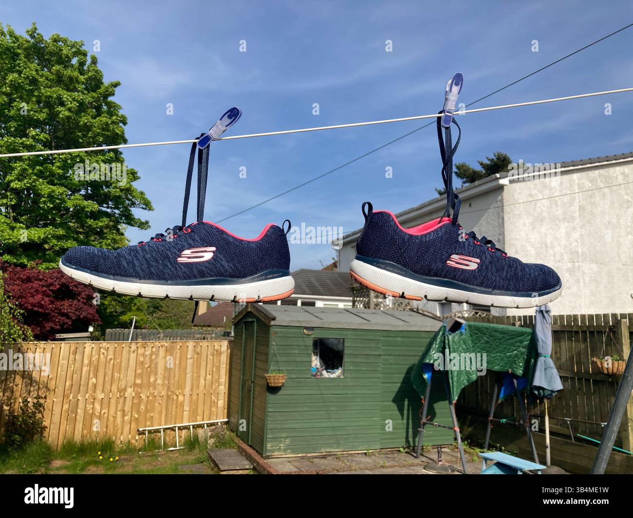 Coppia di Skecher appesi su una linea di lavaggio da giardino sul retro per asciugare dopo essere stati rimossi dalla lavatrice - Immagine stock catturata con smartphone