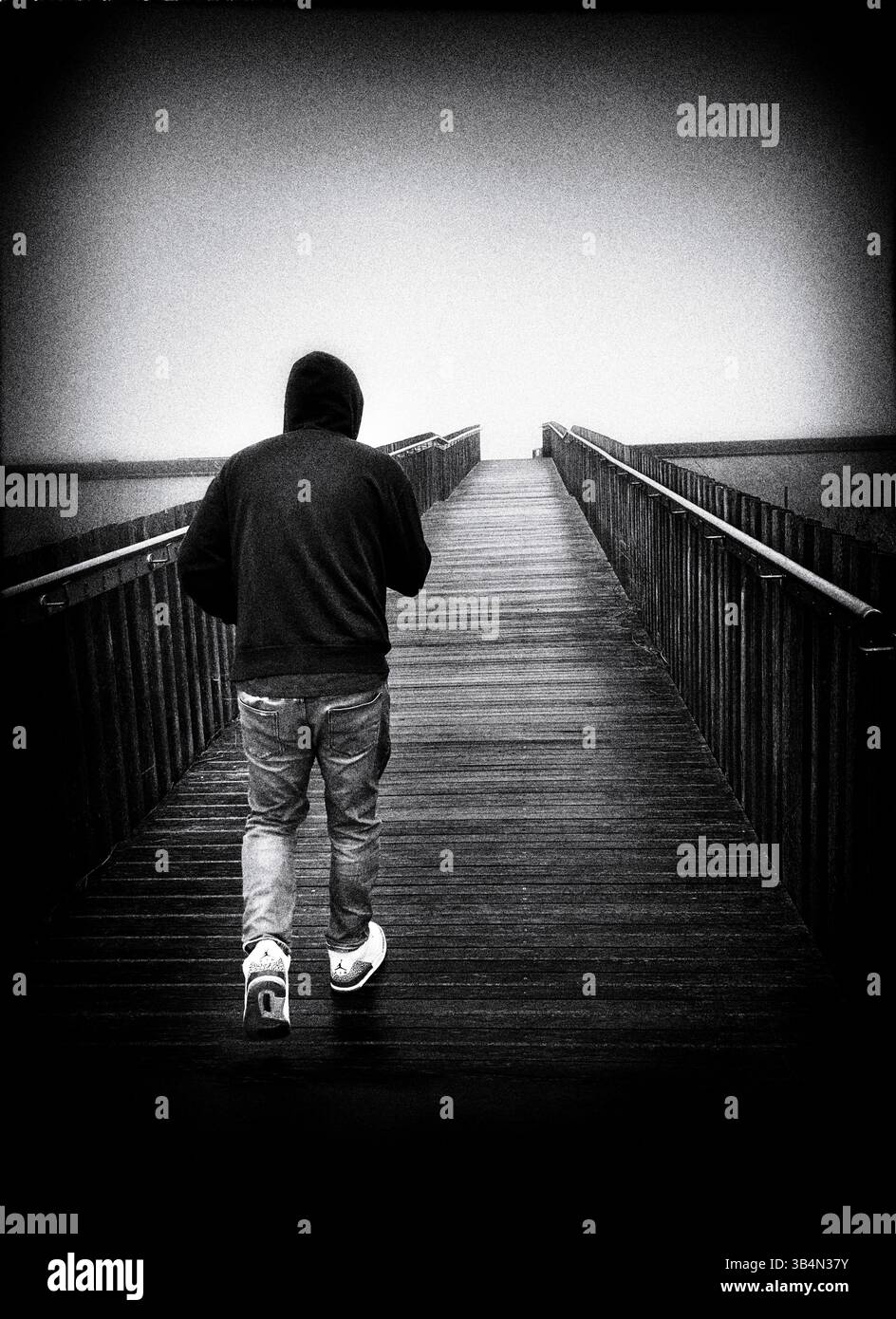 immagine scura e sgranata di un uomo con cappuccio, allontanandosi dalla macchina fotografica sul ponte di legno, lowestoft, suffok, inghilterra Foto Stock