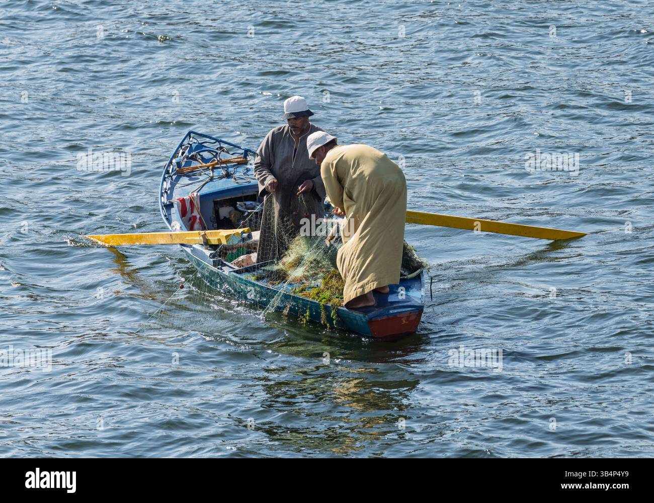 Due uomini in una piccola barca da pesca di legno con pesci catturati nella loro rete dal fiume Nilo Foto Stock