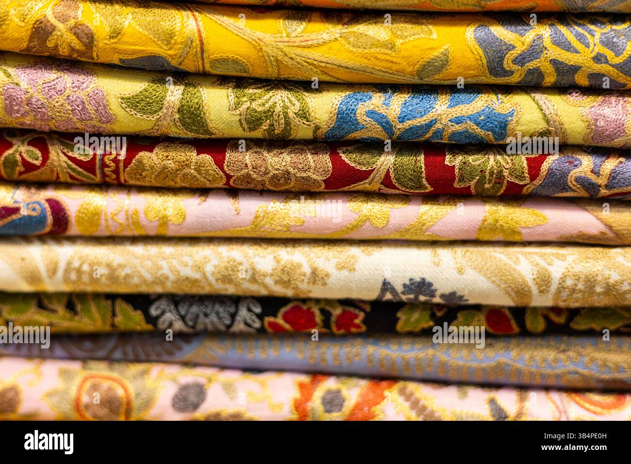 Tessuti dai colori vivaci sono disposti a strati, caratterizzati da ricami dettagliati e motivi floreali. Questo vivace espositore si trova in un negozio tessile Foto Stock