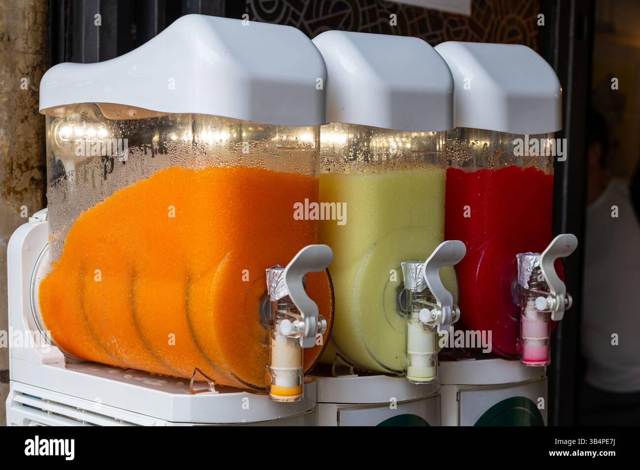 Tre grandi distributori offrono una vasta gamma di bevande colorate, tra cui arancio, verde e rosso, invitanti passanti per gustare dolcetti rinfrescanti Foto Stock