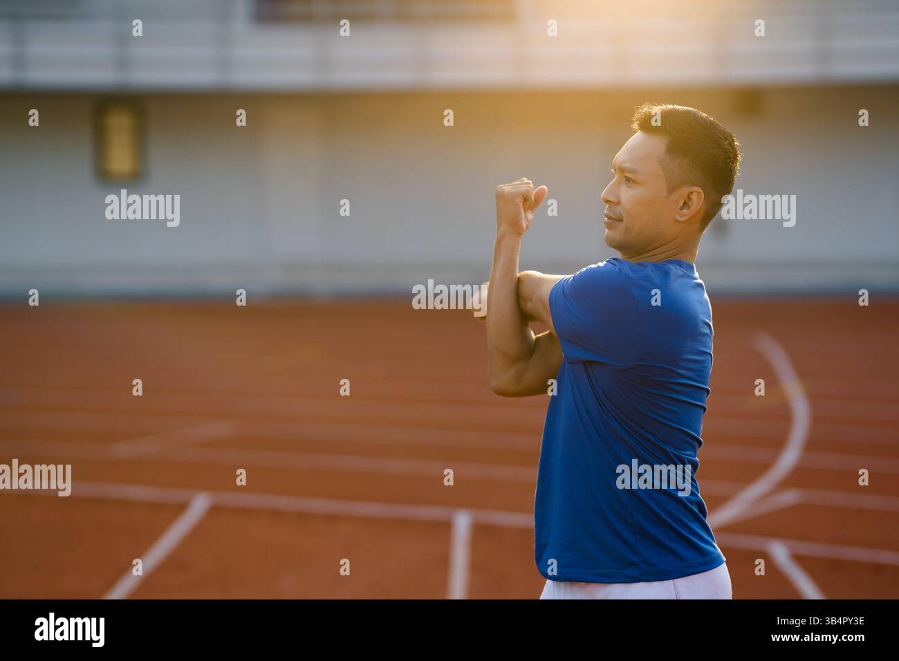 Un uomo asiatico in maglietta blu si allunga i muscoli di braccio e spalle sul circuito dello stadio sportivo. Jogging o corsa, attività all'aperto o lavoro Foto Stock Un uomo asiatico in maglietta blu si allunga i muscoli di braccio e spalle sul circuito dello stadio sportivo. Jogging o corsa, attività all'aperto o lavoro Foto Stock