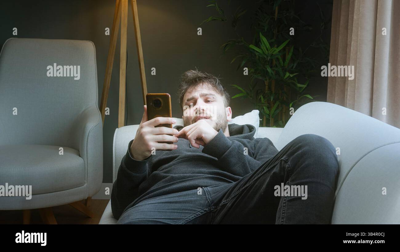 Giovane stanco di guardare brevi video per telefono, sentendosi sprecato tempo Foto Stock