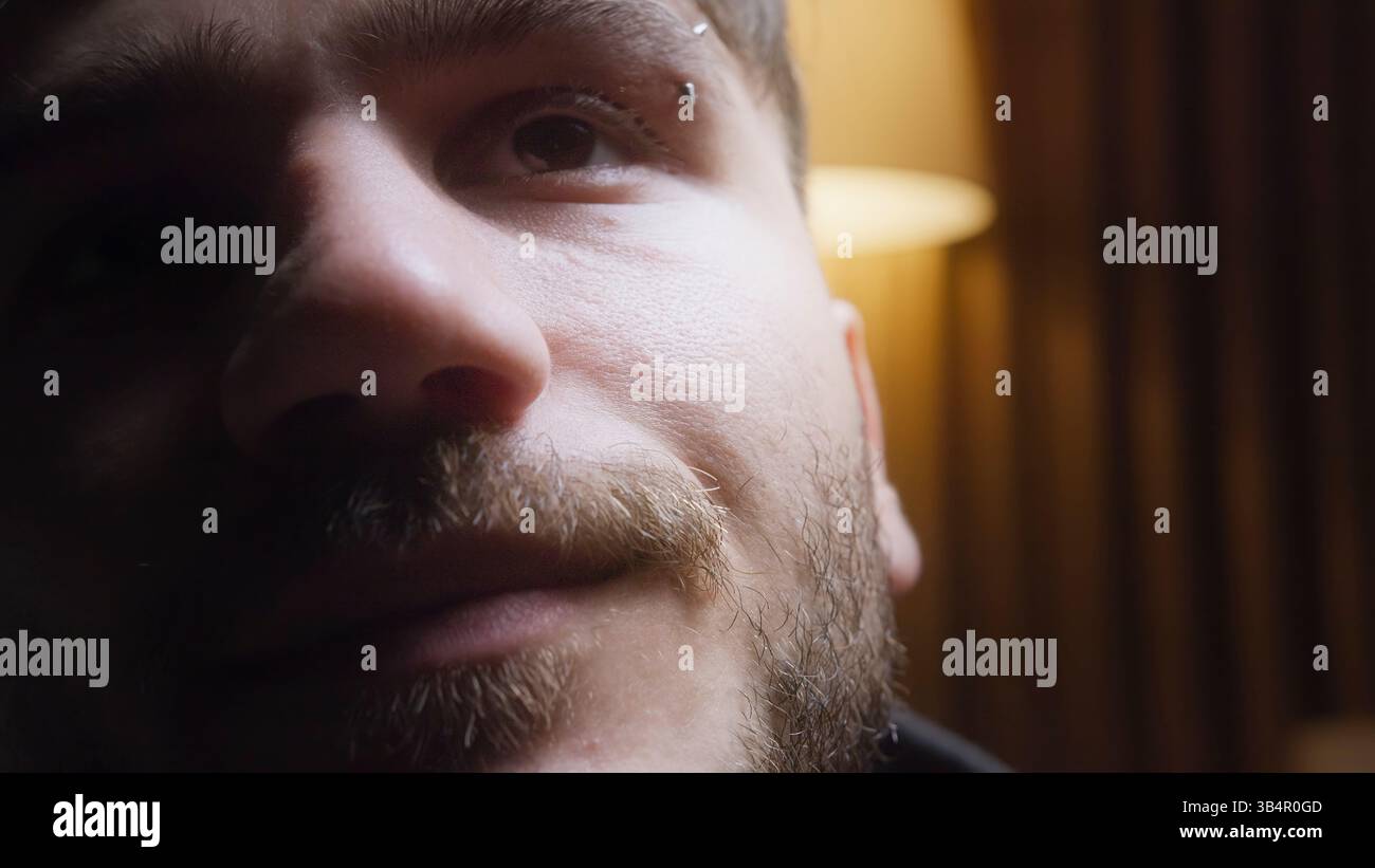 Primo piano di un giovane mans espressione attenta nell'illuminazione soffusa, che mette in risalto emozioni e dettagli del viso in una stanza poco illuminata Foto Stock