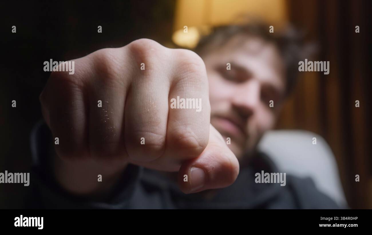 Giovane uomo che mostra il pugno verso la fotocamera in movimento lento con sfondo sfocato Foto Stock