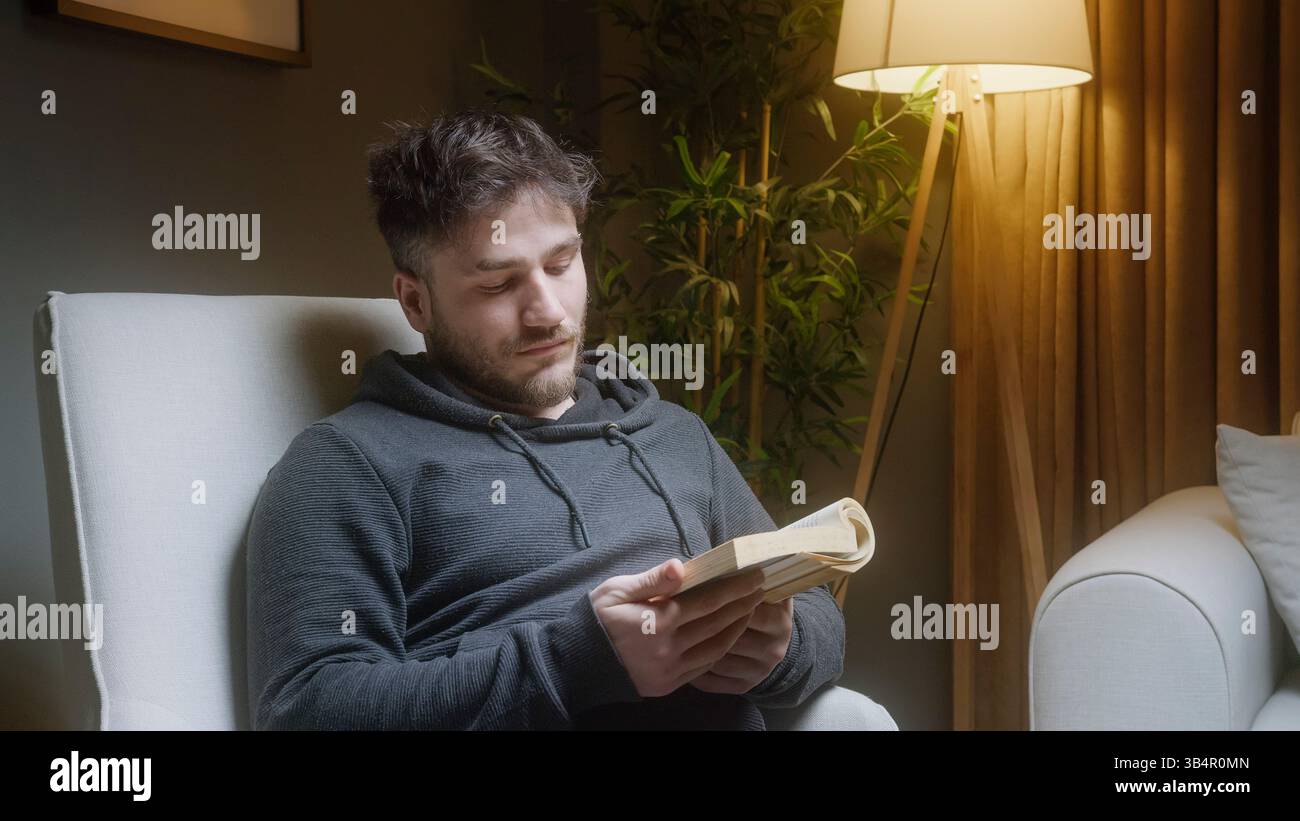 Un uomo che dorme tranquillamente in poltrona dopo aver letto un libro di notte Foto Stock