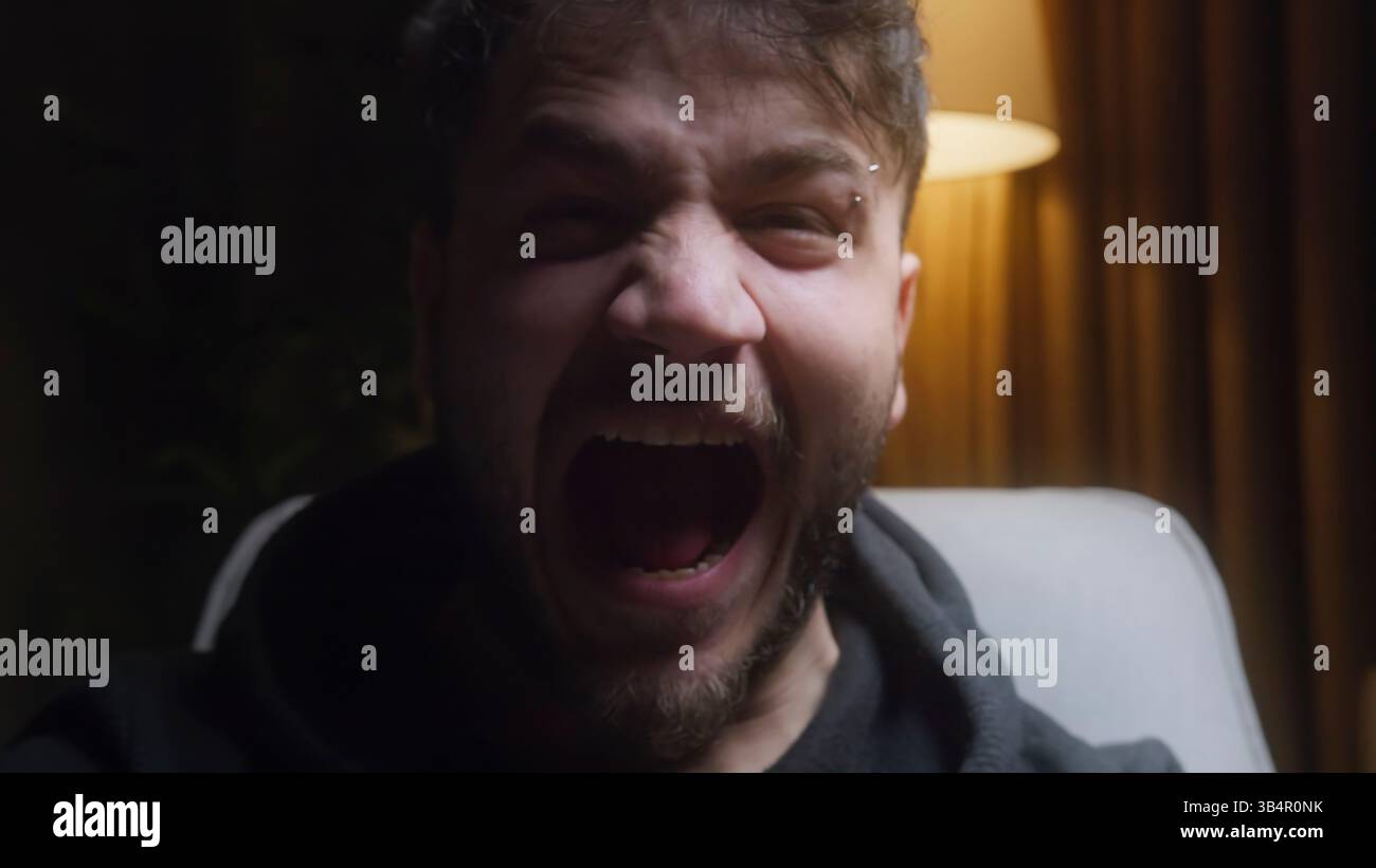 Young Man urla intensamente in una stanza poco illuminata Raw Emotion e Anger Expression Foto Stock