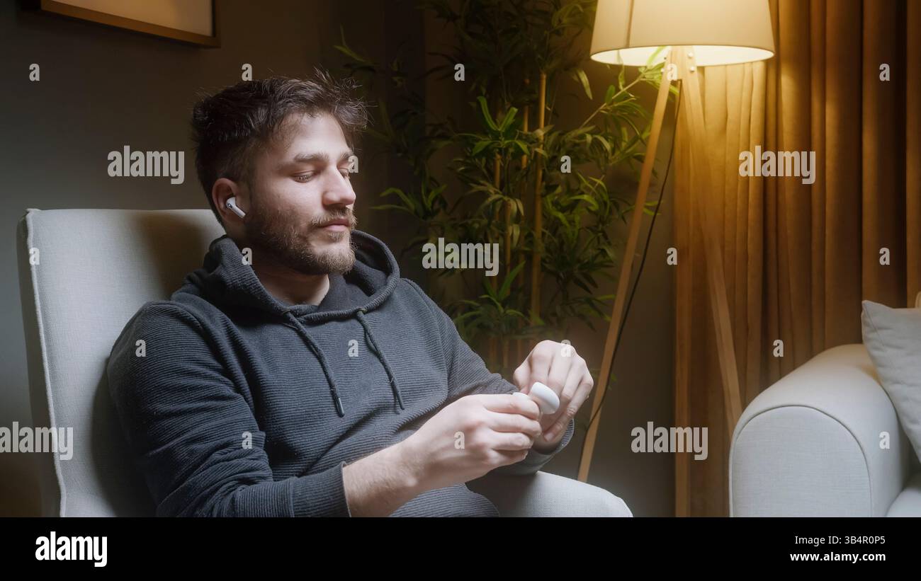 Giovane uomo che si rilassa e ascolta la musica con gli auricolari wireless di notte Foto Stock