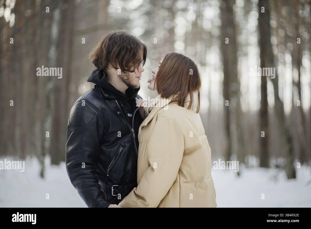 Un momento romantico tra una coppia in una foresta innevata, condividendo vicinanza e calore Foto Stock