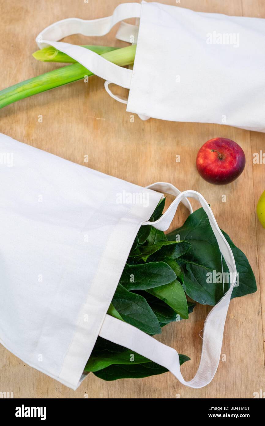 Prodotti freschi come spinaci e porri sono racchiusi in borse riutilizzabili che incarnano la spesa eco-consapevole Foto Stock