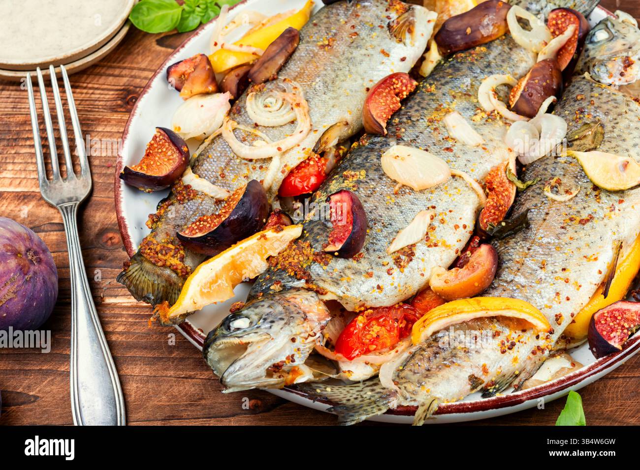 Pesce di trota al forno, servito con fichi arrostiti e limone su un tavolo rustico di legno. Foto Stock
