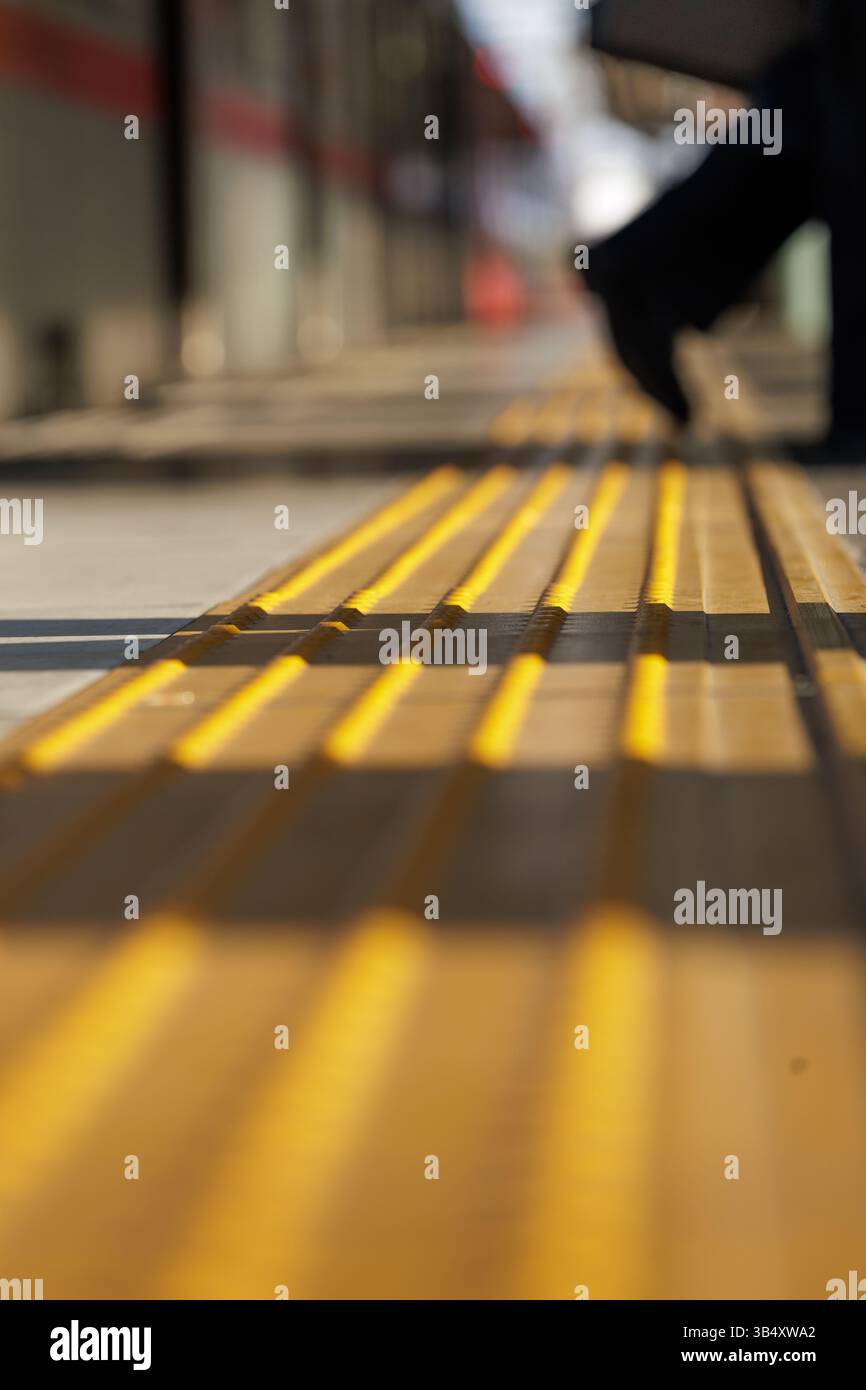 Primo piano di pavimentazione tattile a strisce gialle sulla piattaforma della stazione ferroviaria, progettata per guidare i non vedenti e sottolineare gli elementi urbani. Foto Stock