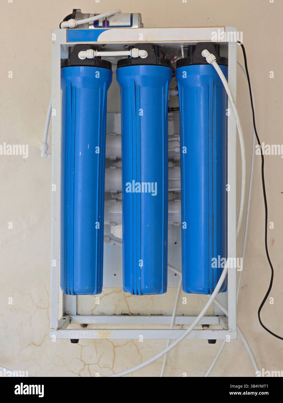 Primo piano di un purificatore d'acqua a tre stadi con alloggiamenti del filtro blu e tubi bianchi collegati su una parete - Immagine stock catturata con smartphone