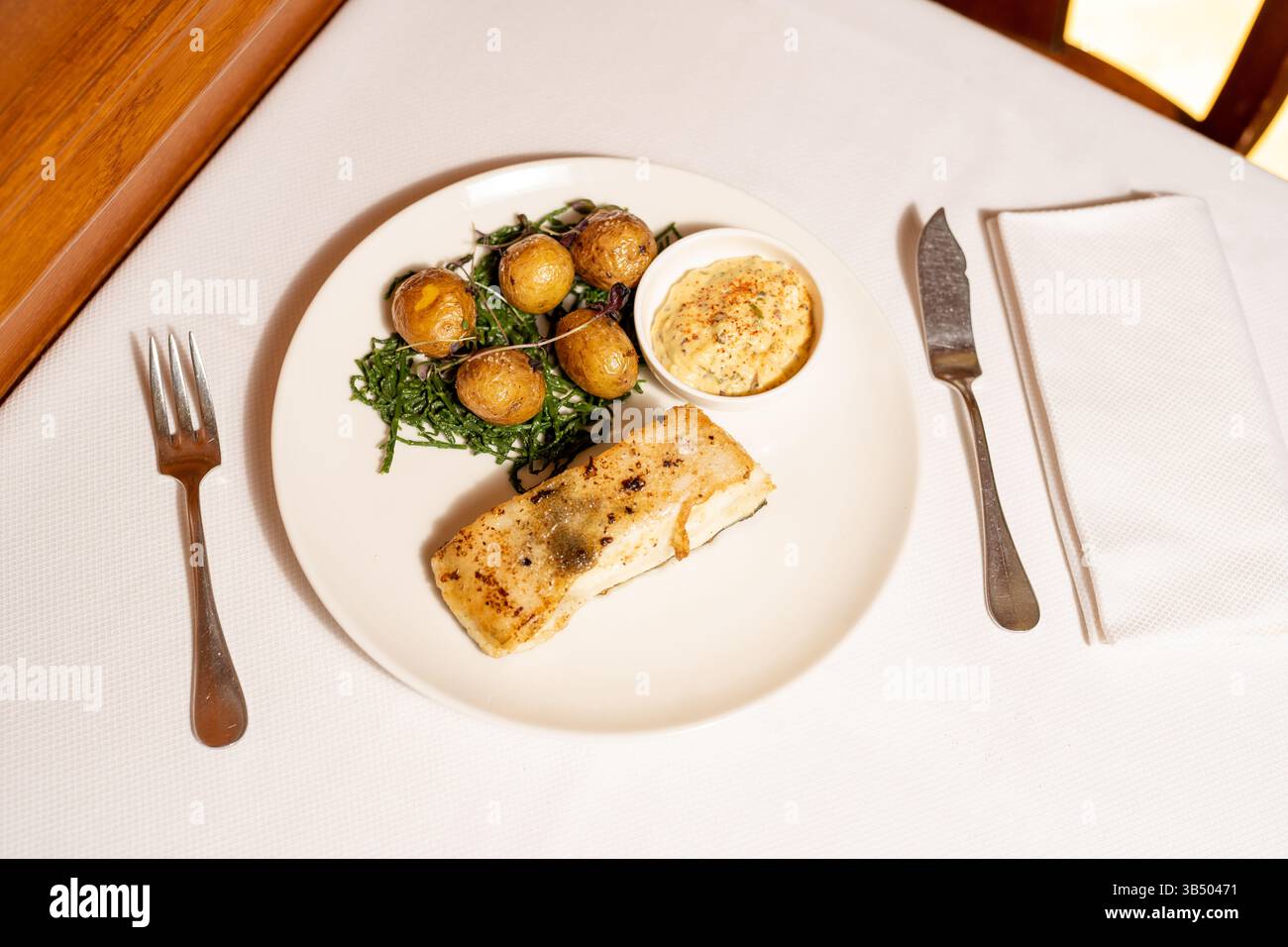 Elegante pesce e patate arrostite: Piatti gourmet con verdure fresche e salsa Foto Stock