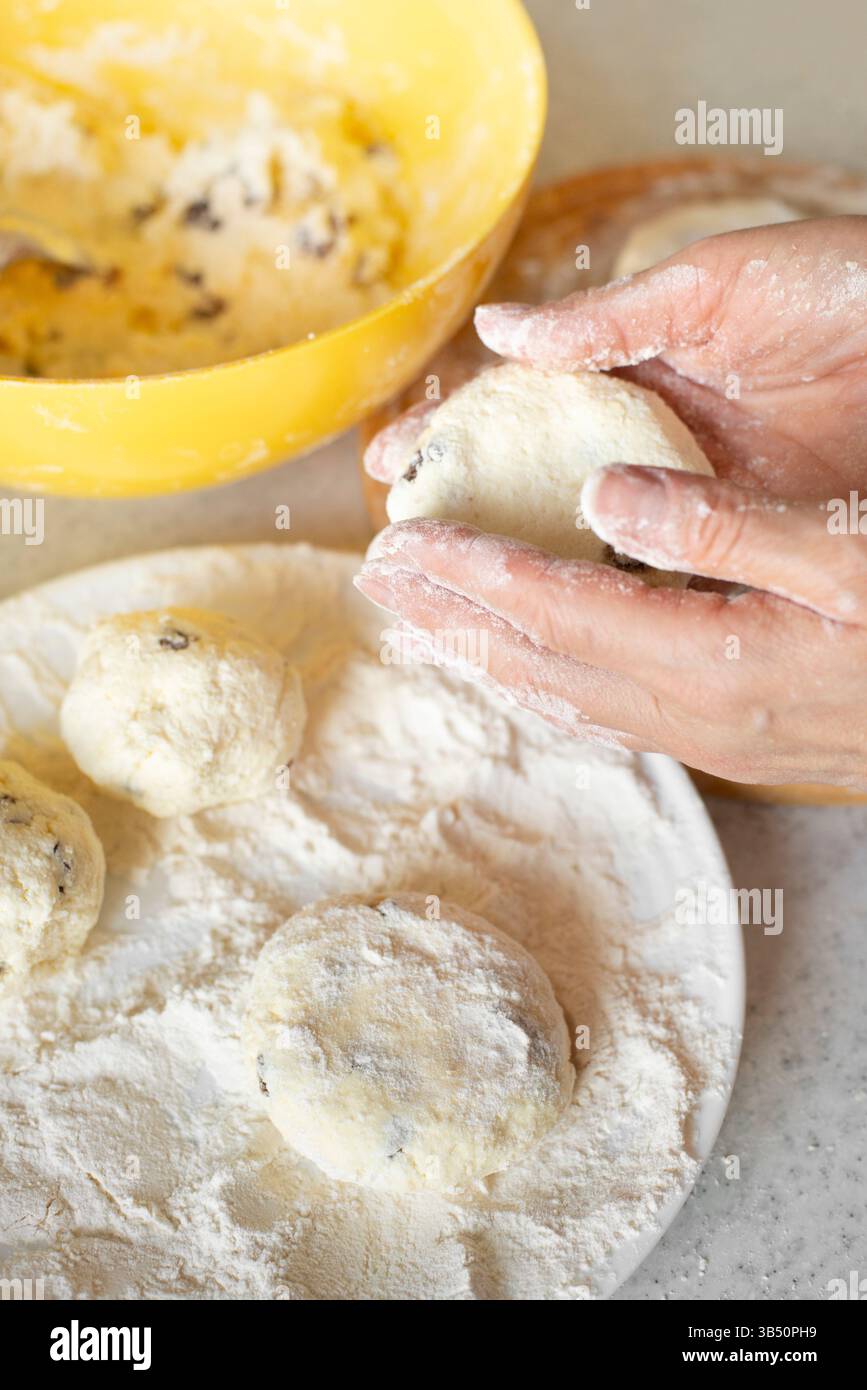Le mani caucasiche preparano frittelle di formaggio fresco con uvetta Foto Stock