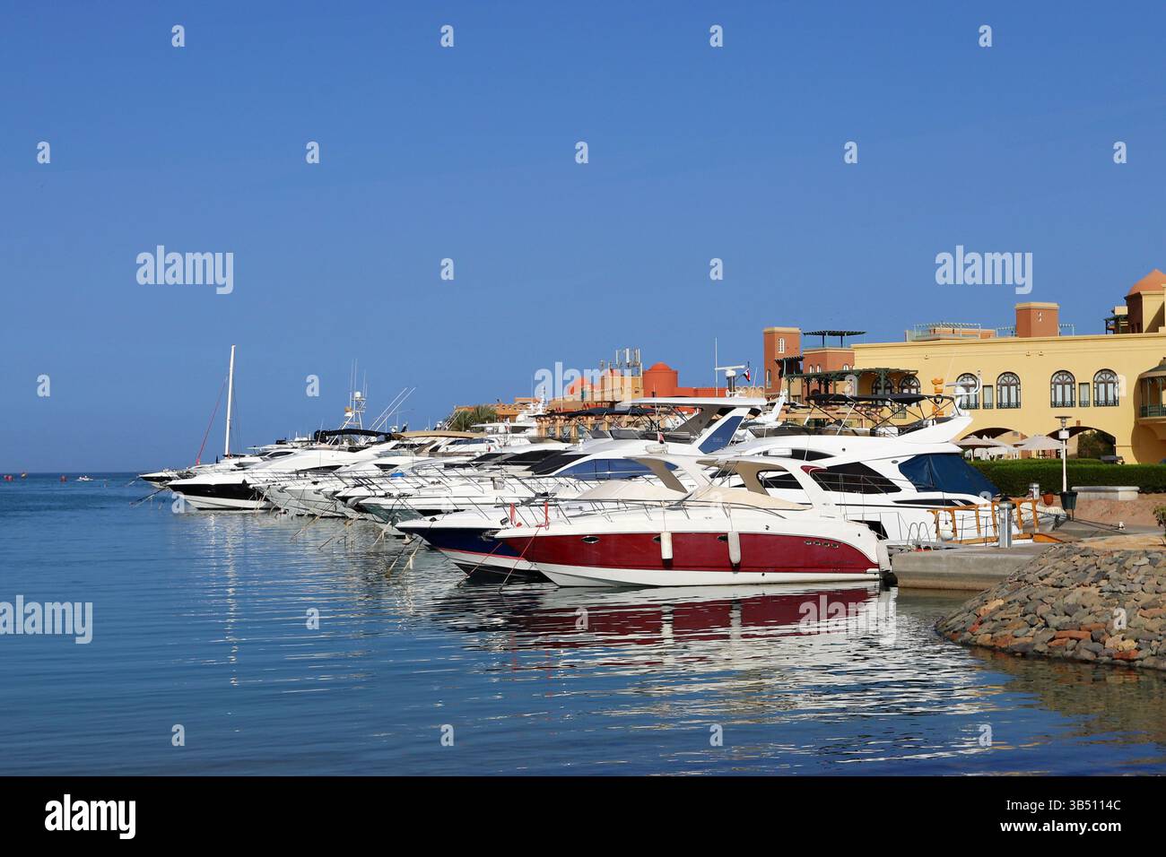 Yacht di lusso attraccati in un porticciolo di El Gouna, in Egitto, con il cielo azzurro e gli edifici sul lungomare che si riflettono nelle calme acque del Mar Rosso. Foto Stock