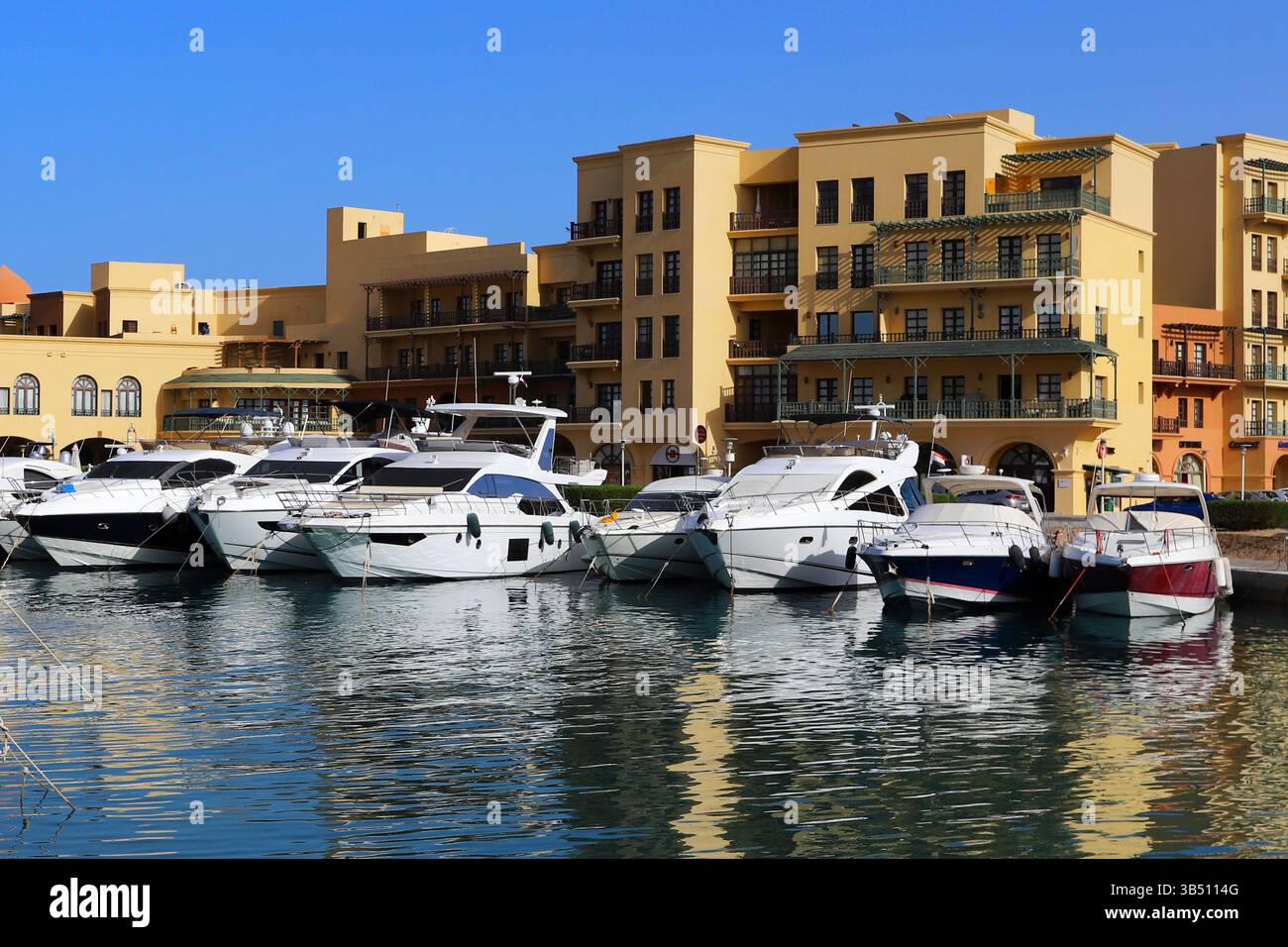 Yacht di lusso attraccati in un porticciolo di El Gouna, in Egitto, con il cielo azzurro e gli edifici sul lungomare che si riflettono nelle calme acque del Mar Rosso. Foto Stock