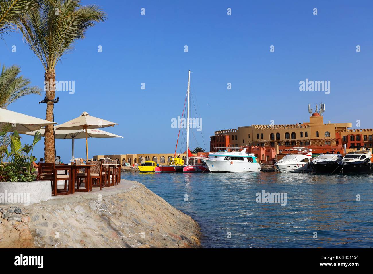 Yacht di lusso attraccati in un porticciolo di El Gouna, in Egitto, con il cielo azzurro e gli edifici sul lungomare che si riflettono nelle calme acque del Mar Rosso. Foto Stock