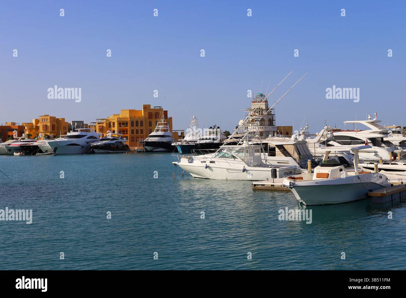 Yacht di lusso attraccati in un porticciolo di El Gouna, in Egitto, con il cielo azzurro e gli edifici sul lungomare che si riflettono nelle calme acque del Mar Rosso. Foto Stock