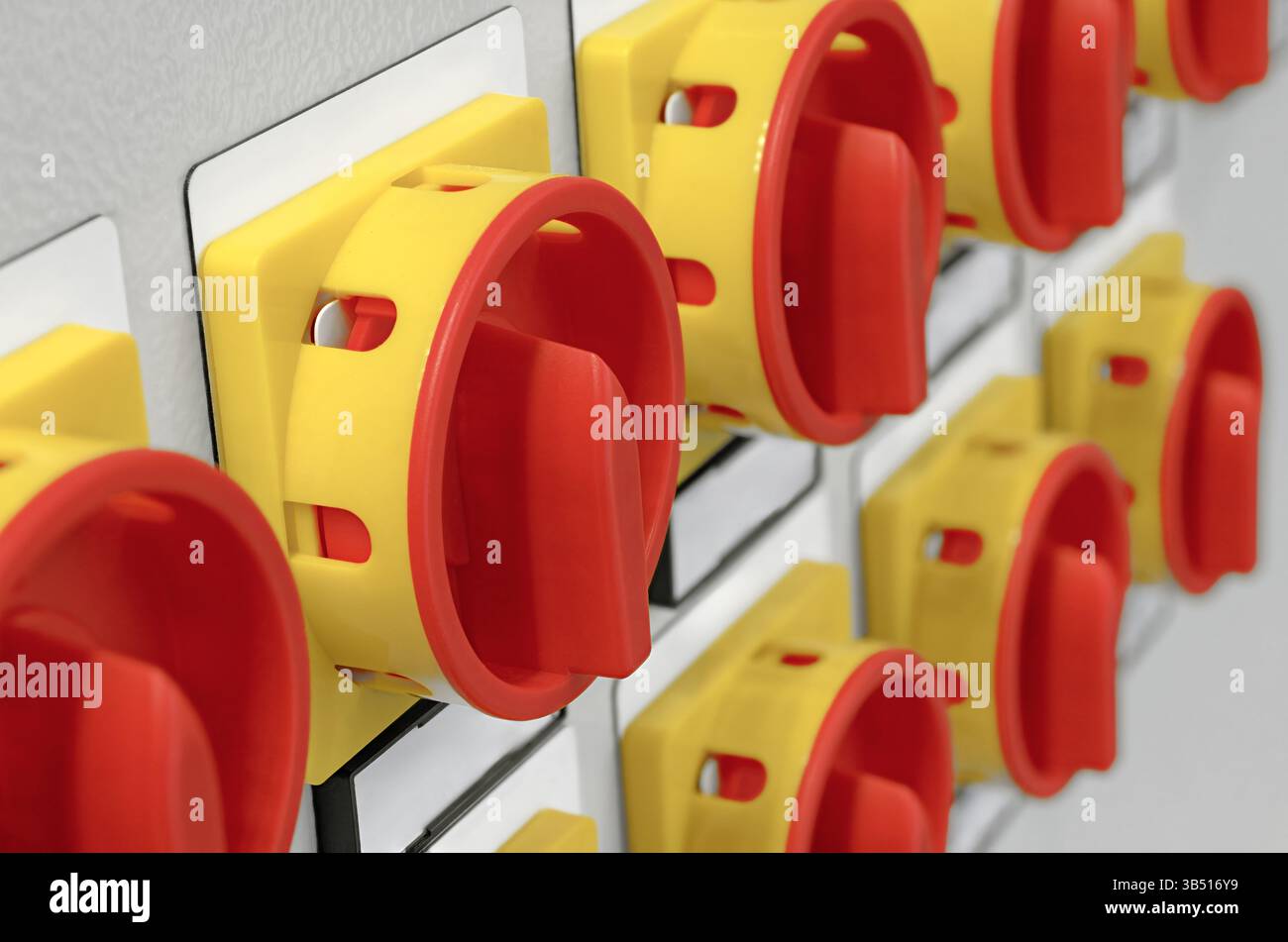 Molti interruttori elettrici rossi e gialli con etichette bianche su un pannello di controllo grigio. Background industriale astratto. Foto Stock