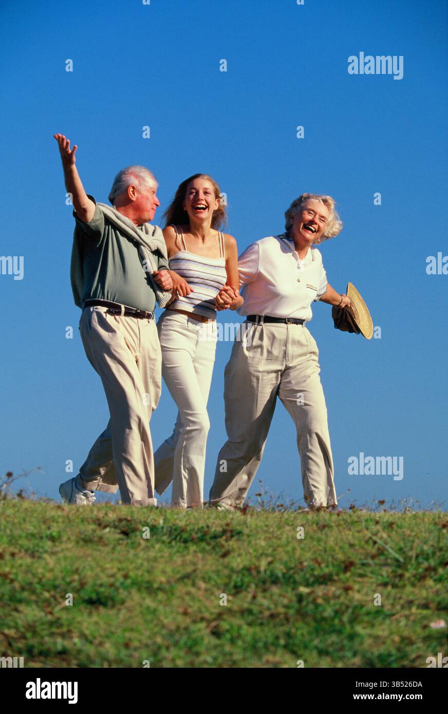 Coppia senior con figlia adulta che cammina all'aperto su una collina erbosa. Foto Stock