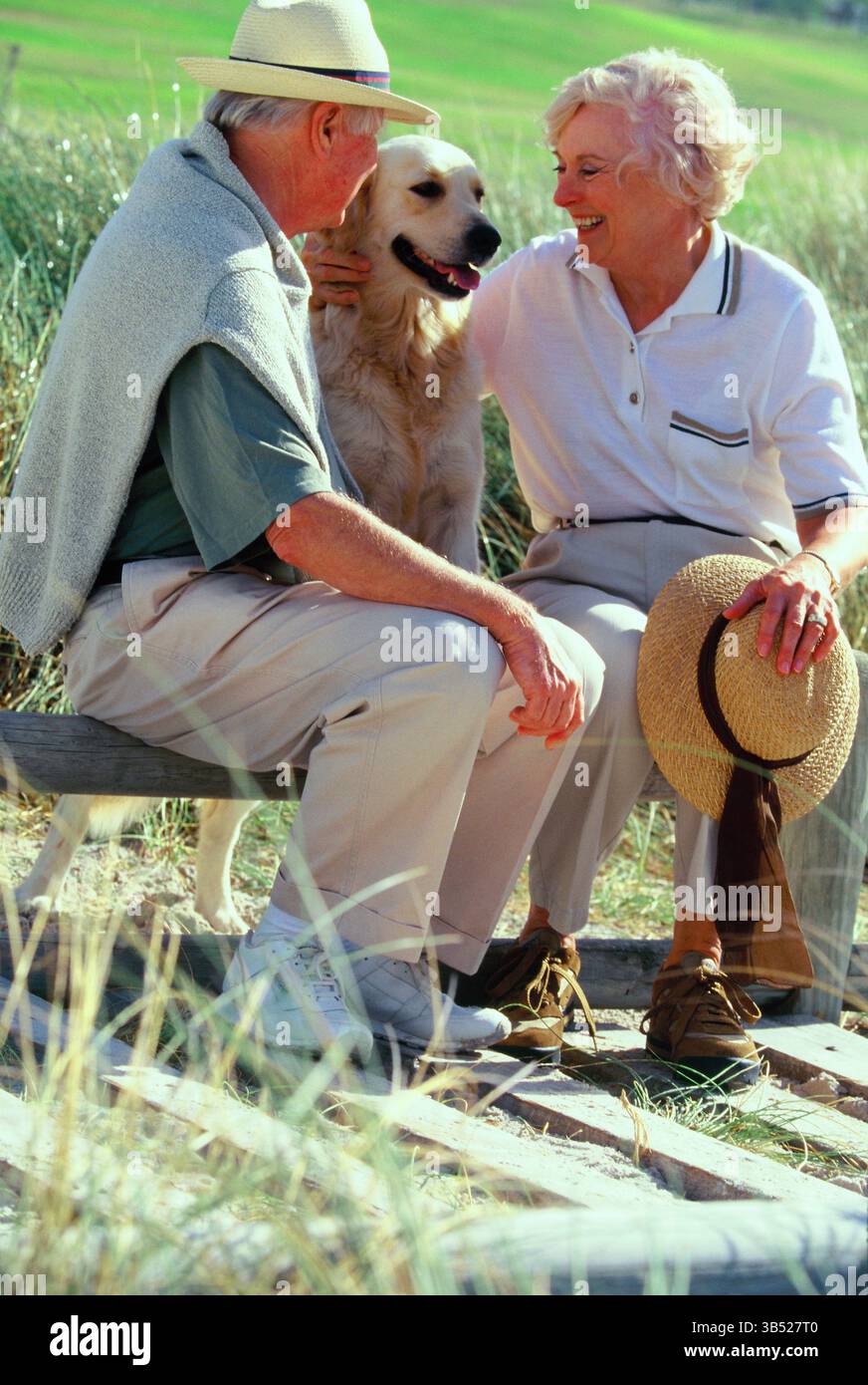 Uomo e donna senior con cane Labrador seduto all'aperto sulla panchina del parco. Foto Stock