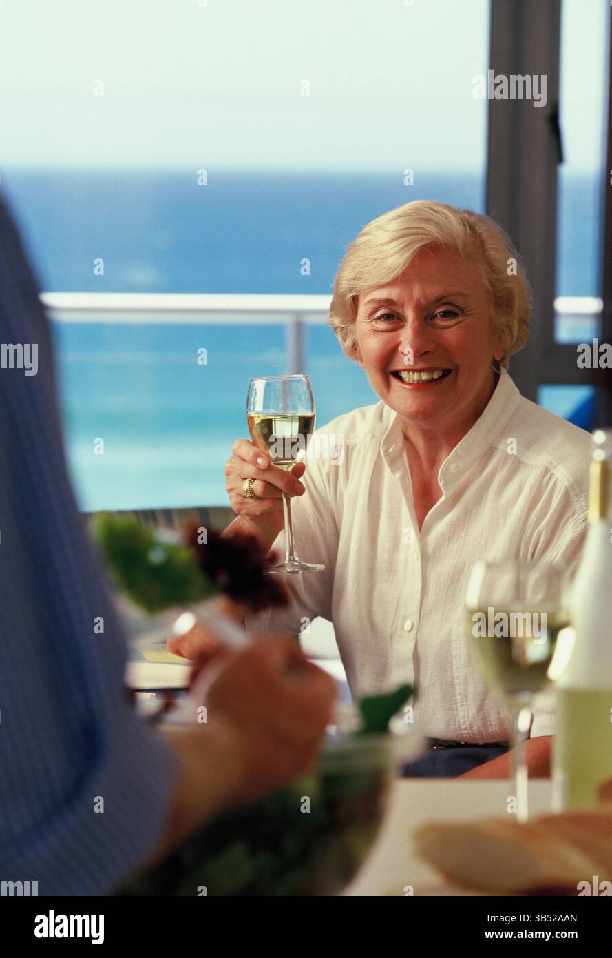 Donna anziana che beve vino nel ristorante con vista sul mare. Foto Stock