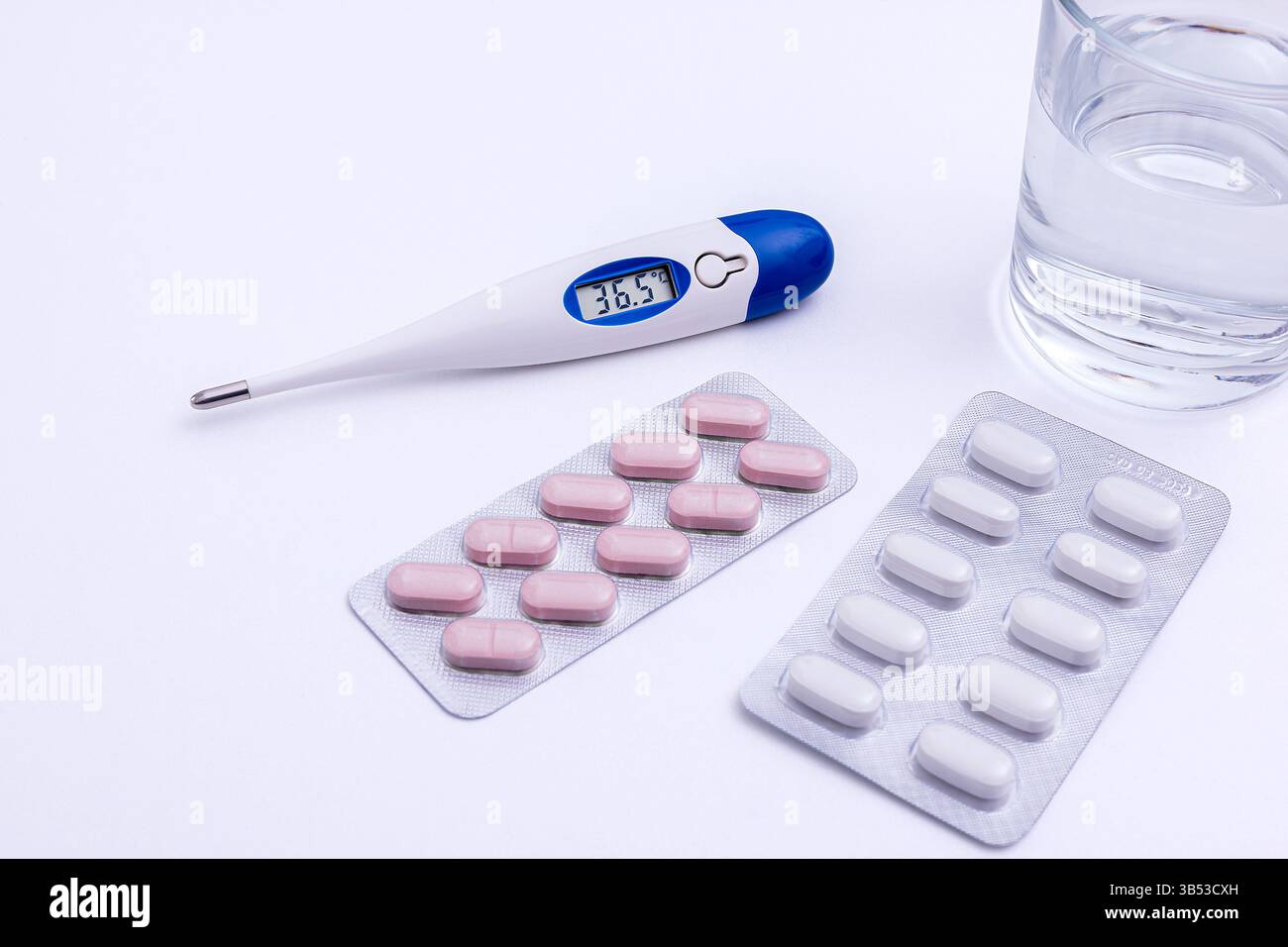 Termometro, medicinali e bicchiere d'acqua su un tavolo. Foto Stock