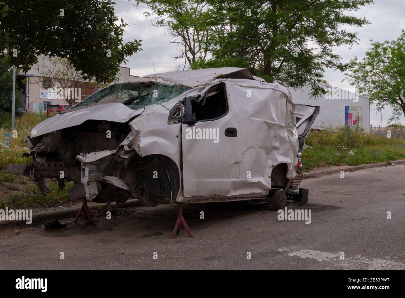 Furgone bianco rotto con ruote mancanti e carrozzeria danneggiata, appoggiato su cavalletti per assali in una zona industriale Foto Stock