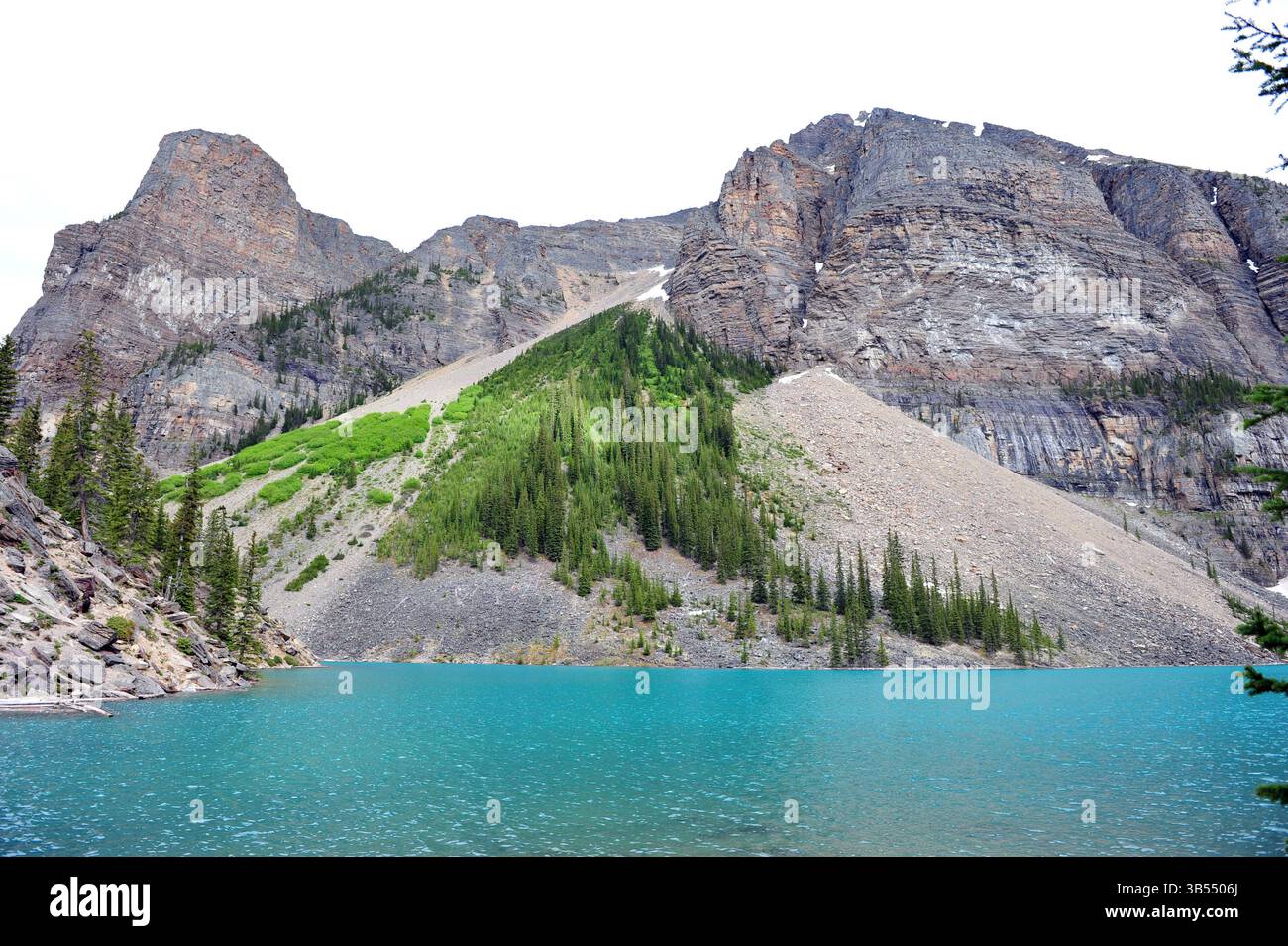 Montagne rocciose e lago turchese nel Parco Nazionale di Banff, Alberta, Canada, con foresta alpina e ripidi pendii di ghiaia sotto la luce del giorno. Foto Stock