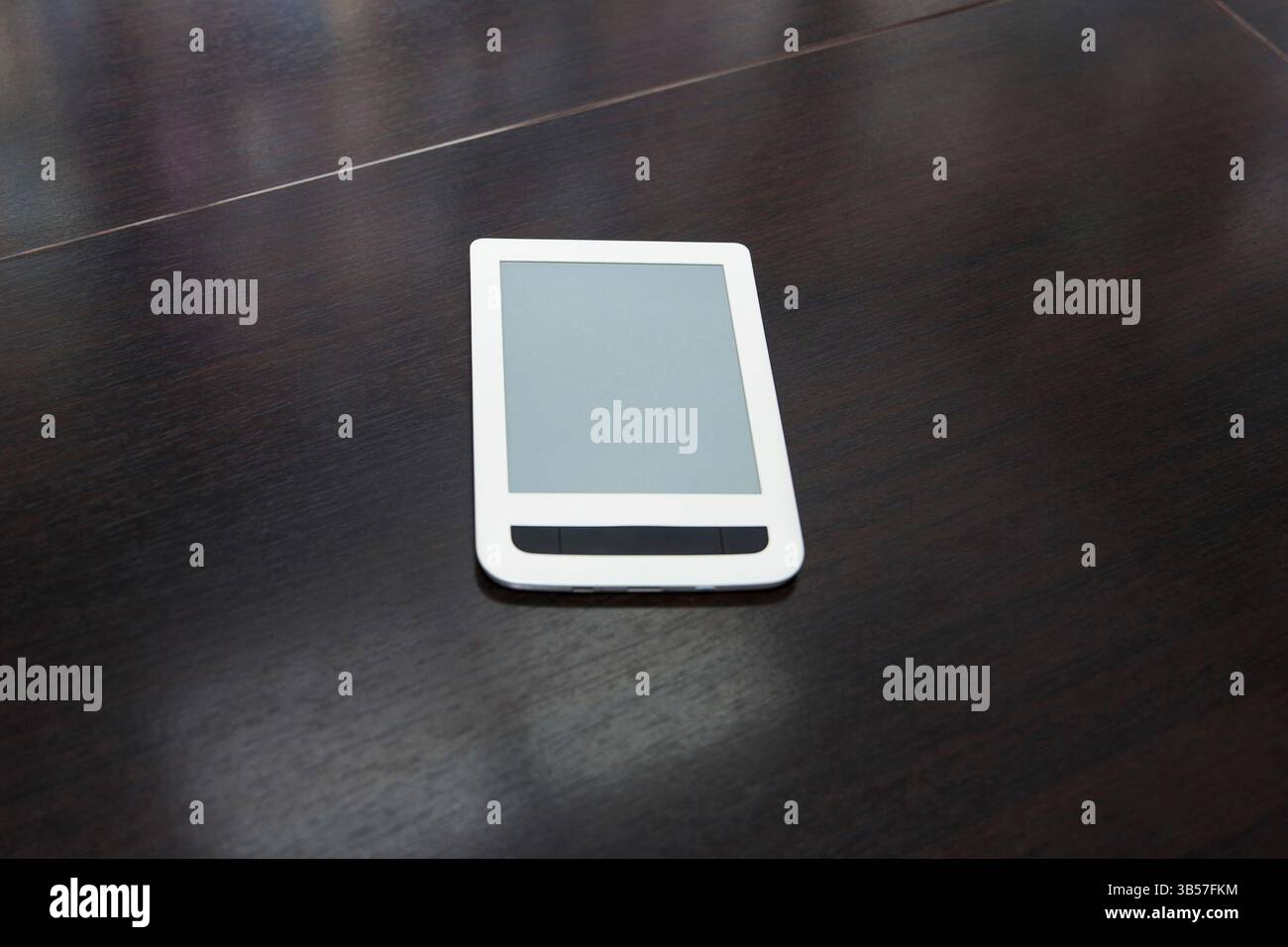 E-Reader bianco con schermo vuoto appoggiato su un tavolo di legno scuro, realistico stile fotografico, sfondo minimo per ufficio, concetto di lettura digitale Foto Stock