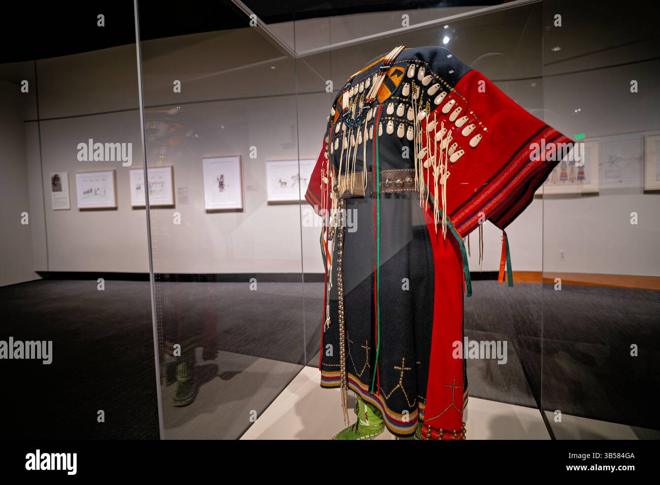 WASHINGTON DC - Kiowa Battle Dress creato intorno al 2000 dall'artista Vanessa Jennings (Kiowa/Pima, B. 1952) esposto al National Museum of the American Indian. Questo moderno abito cerimoniale include un abito realizzato in lana rossa e blu arcobaleno con imitazioni di denti di alce, perle di vetro e patch militari che rappresentano la prima divisione di cavalleria dell'esercito dalla guerra del Vietnam. L'ensemble presenta anche una cintura d'argento tedesca, mocassini con perline e una collana con perline di osso che sarebbe stata indossata dai parenti femminili per onorare i membri della società guerriera Kiowa. Foto Stock