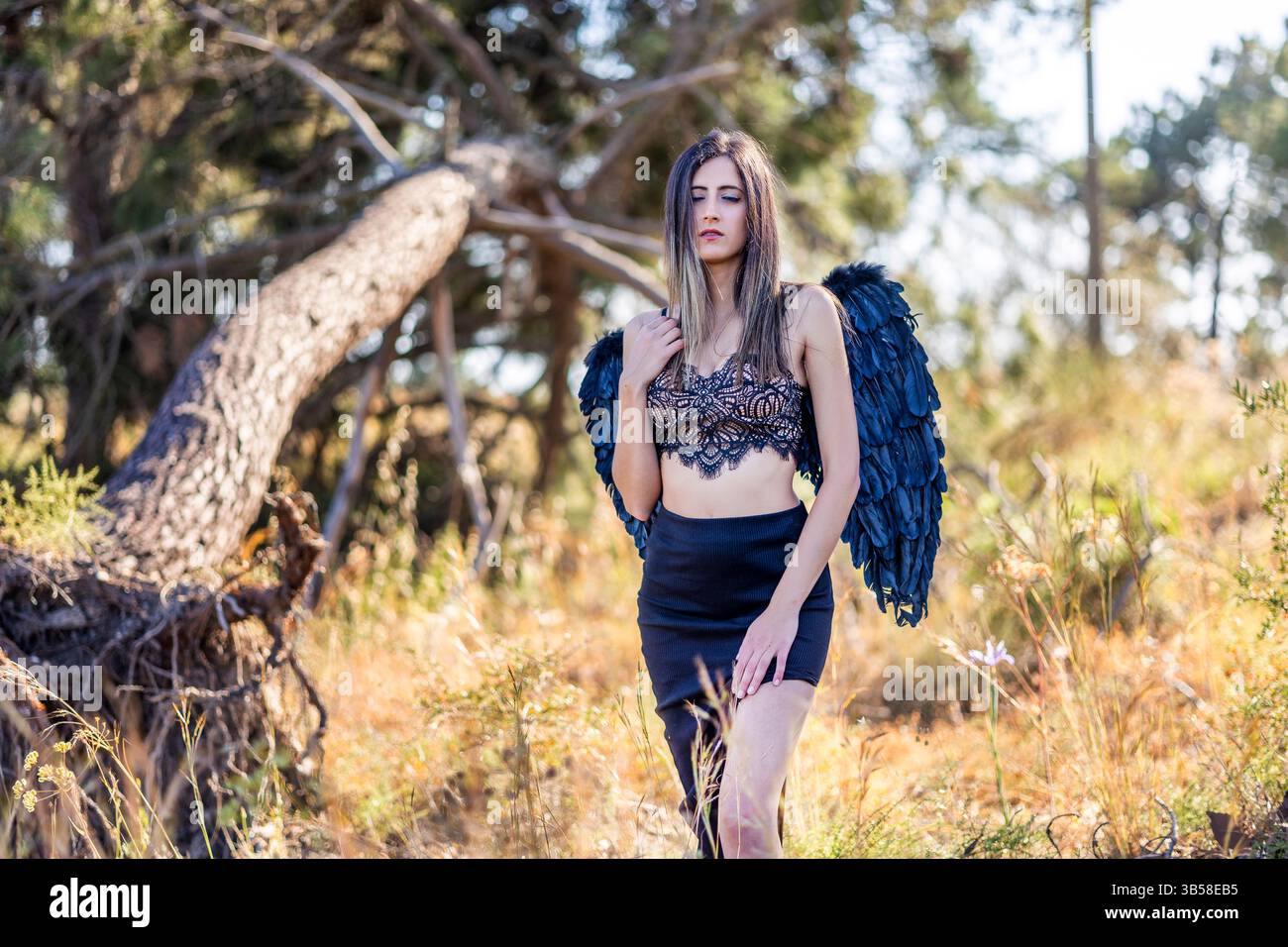 Vista ravvicinata di una bella donna nella foresta che posa con le ali scure, che sembra un angelo scuro. Foto Stock