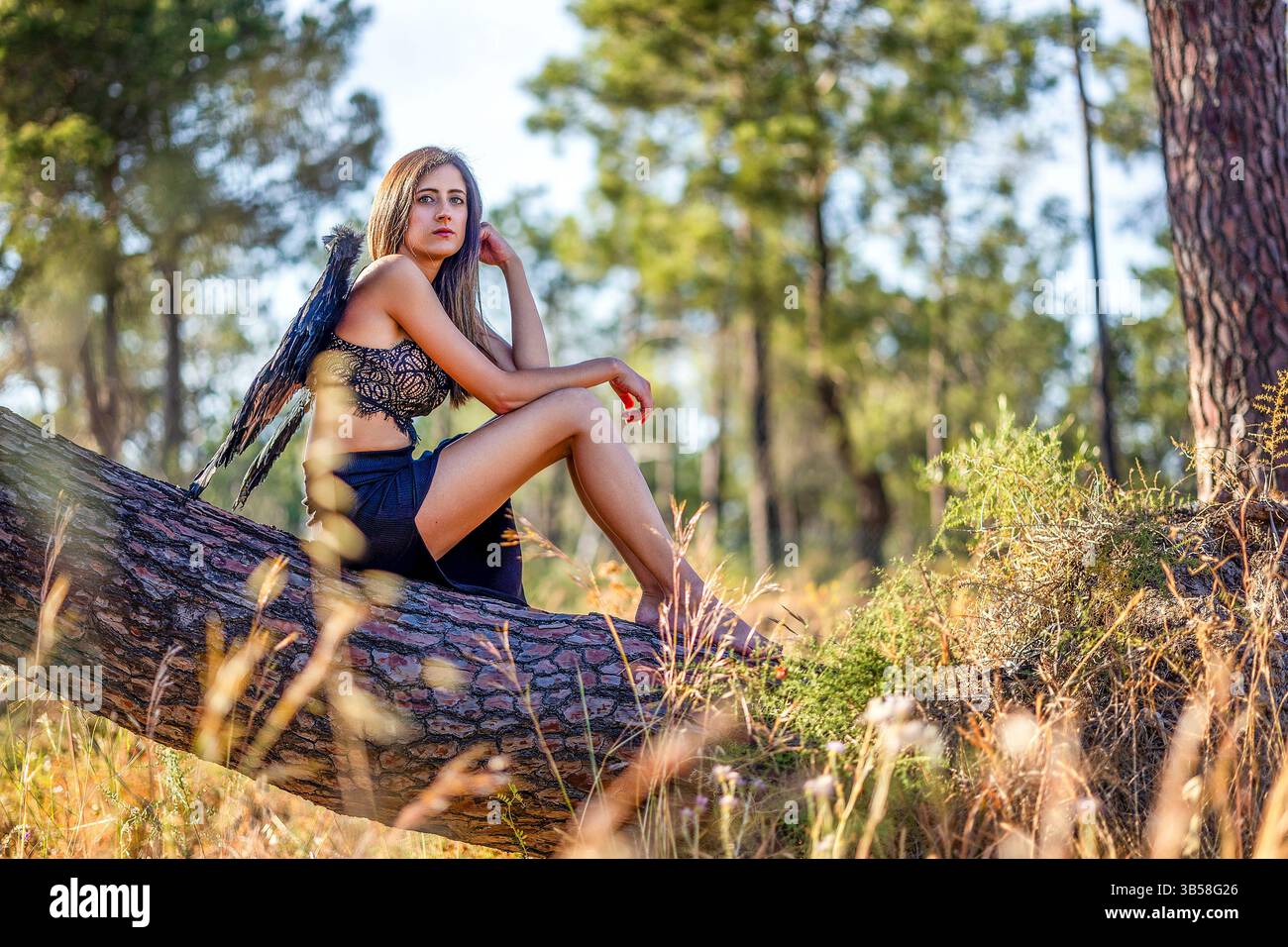 Vista ravvicinata di una bella donna nella foresta che posa con le ali scure, che sembra un angelo scuro. Foto Stock