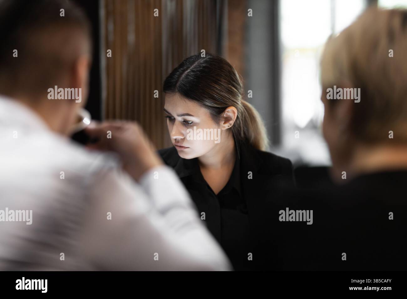 Una giovane donna professionista di affari ascolta attentamente durante un incontro di lavoro serio con altri colleghi in un ufficio moderno. Foto Stock
