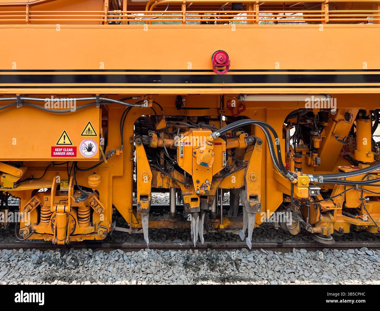Una macchina antimanomissione con zavorra parcheggiata in una stazione ferroviaria, equipaggiata per la manutenzione dei cingoli. Garantisce un allineamento e un livellamento precisi delle guide con ghiaia per Foto Stock