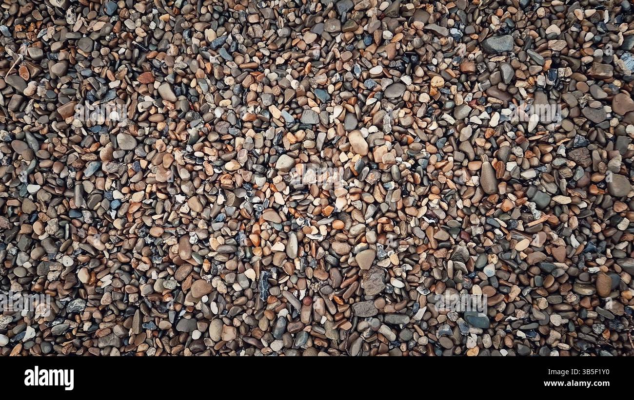 Consistenza di ciottoli bagnati multicolori con rocce di dimensioni e forme diverse. La disposizione naturale evidenzia toni terrosi come abbronzatura, grigio e marrone. Uniforme Foto Stock