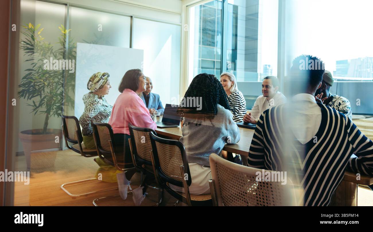 I colleghi partecipano a una dinamica riunione aziendale incentrata sulla collaborazione e il lavoro di squadra in un ambiente luminoso e moderno con ampie finestre Foto Stock