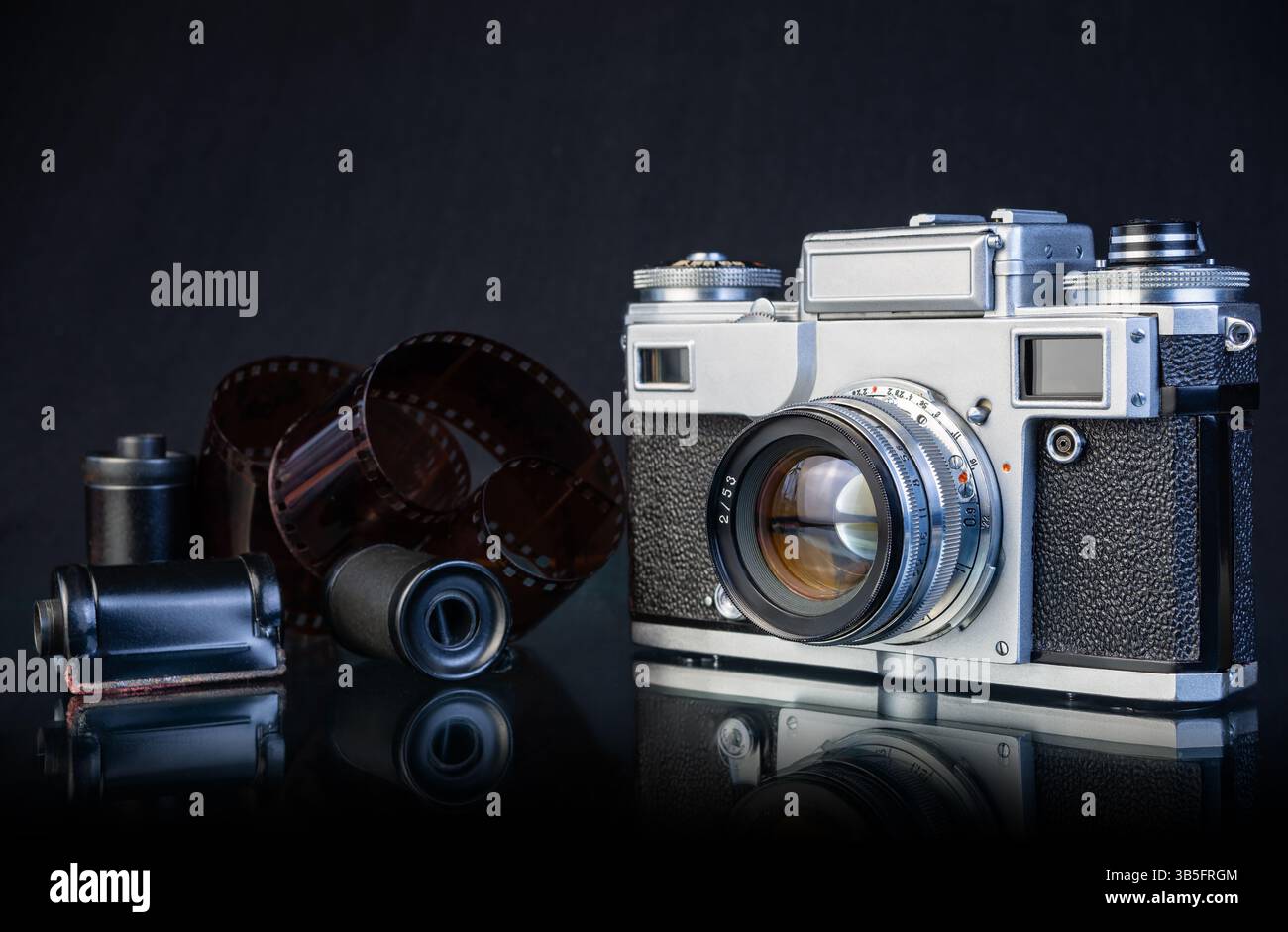 Una fotocamera vintage è posizionata accanto a diversi rulli di pellicola, sottolineando un legame nostalgico con le tecniche fotografiche tradizionali e i ricordi. Foto Stock