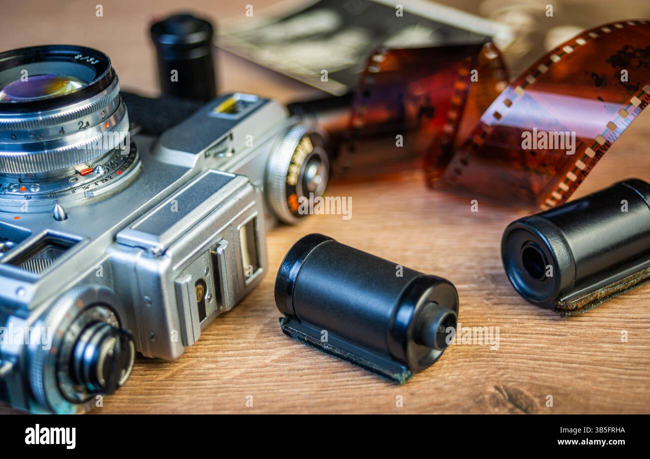 Una macchina fotografica d'epoca poggia su una superficie di legno circondata da fotografie in bianco e nero e rotoli di pellicola, evocando nostalgia per la fotografia classica. Foto Stock
