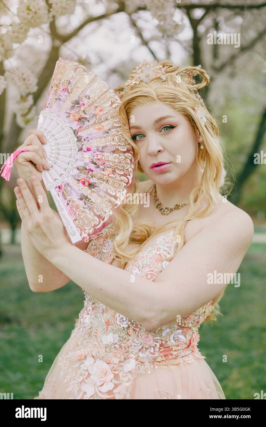 Donna bionda con un fan sullo sfondo dei fiori di ciliegio Foto Stock